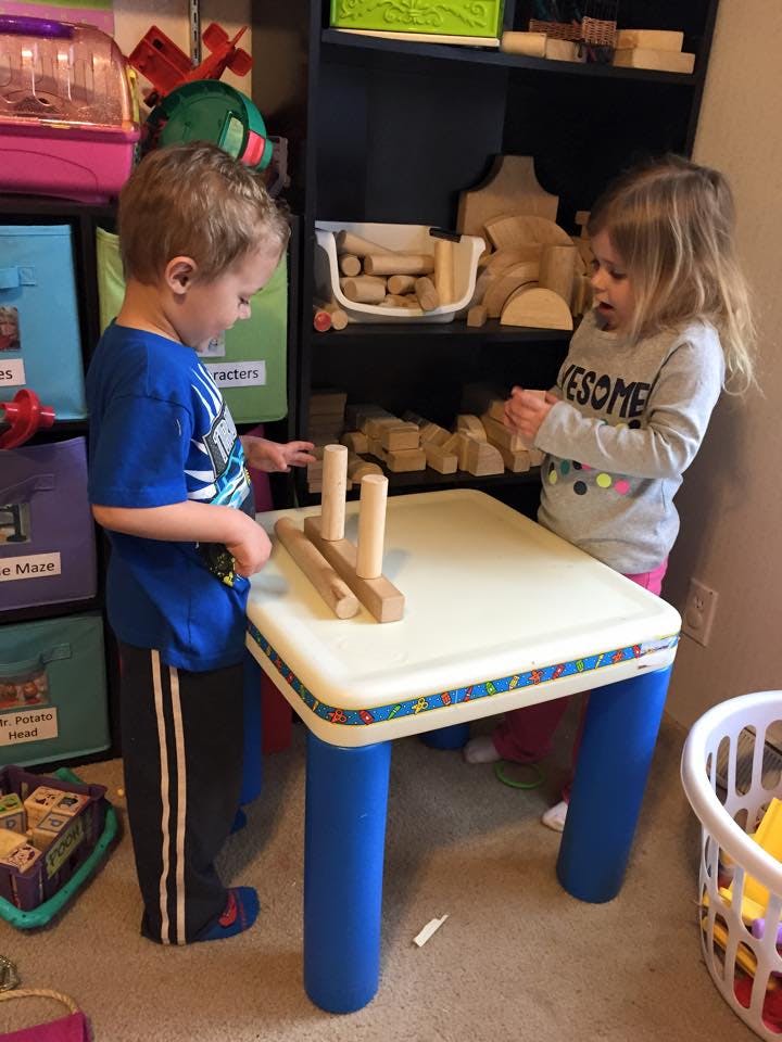 Two children playing with wooden blocks at a small table
