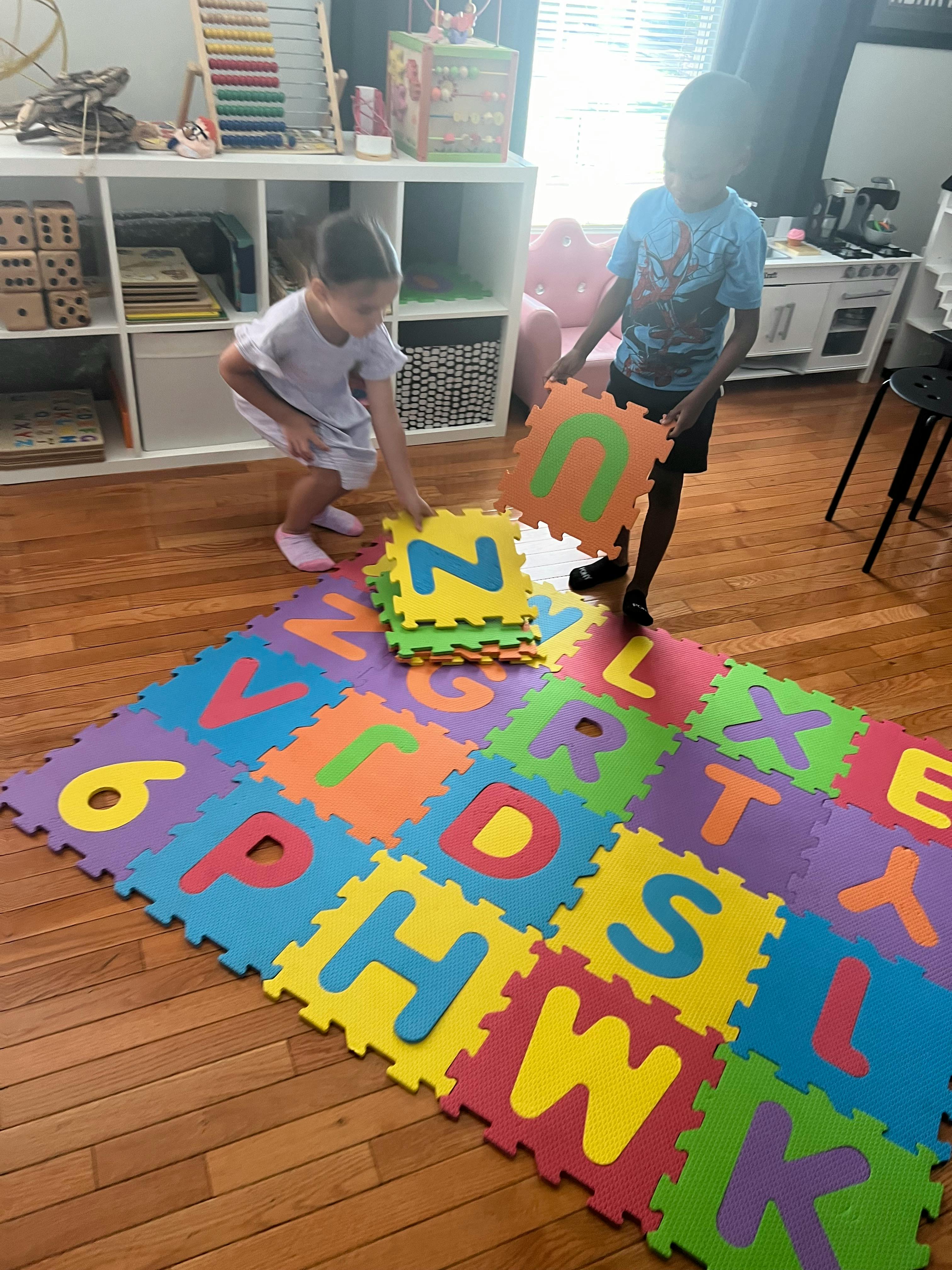Two children playing with colorful alphabet floor mats
