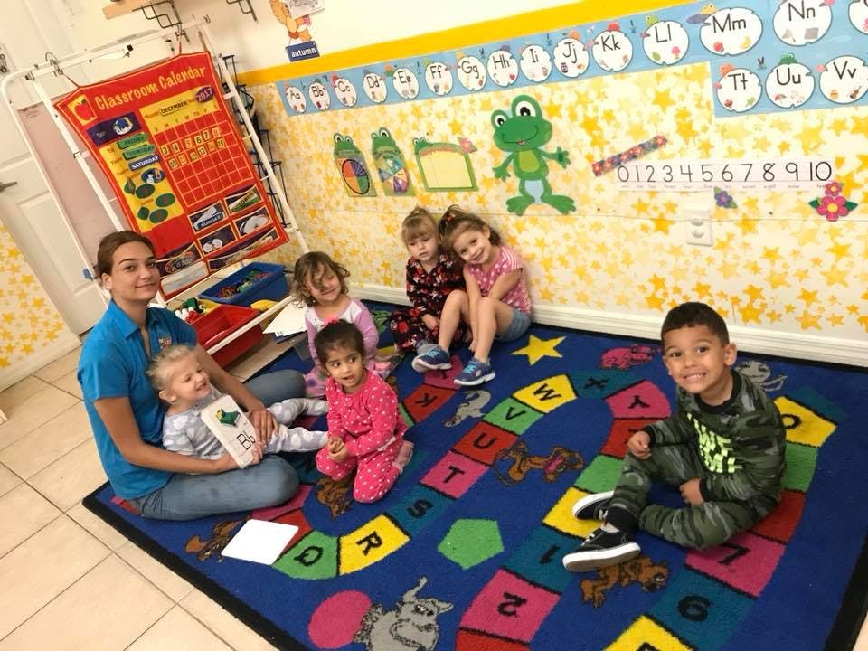 Adult and multiple children sitting on a colorful alphabet rug in a classroom