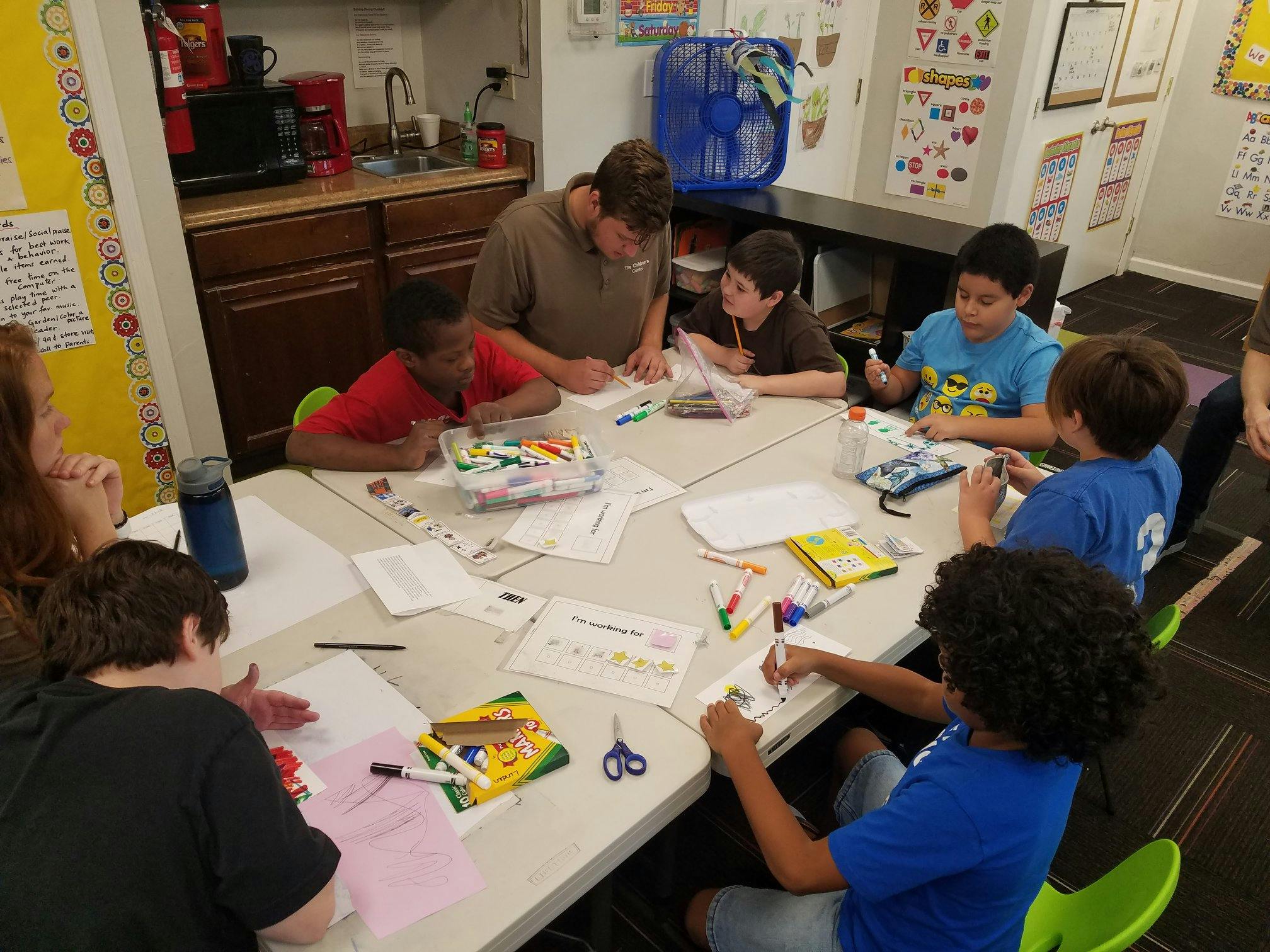 Adult and children sitting around a table doing crafts and looking at schoolwork