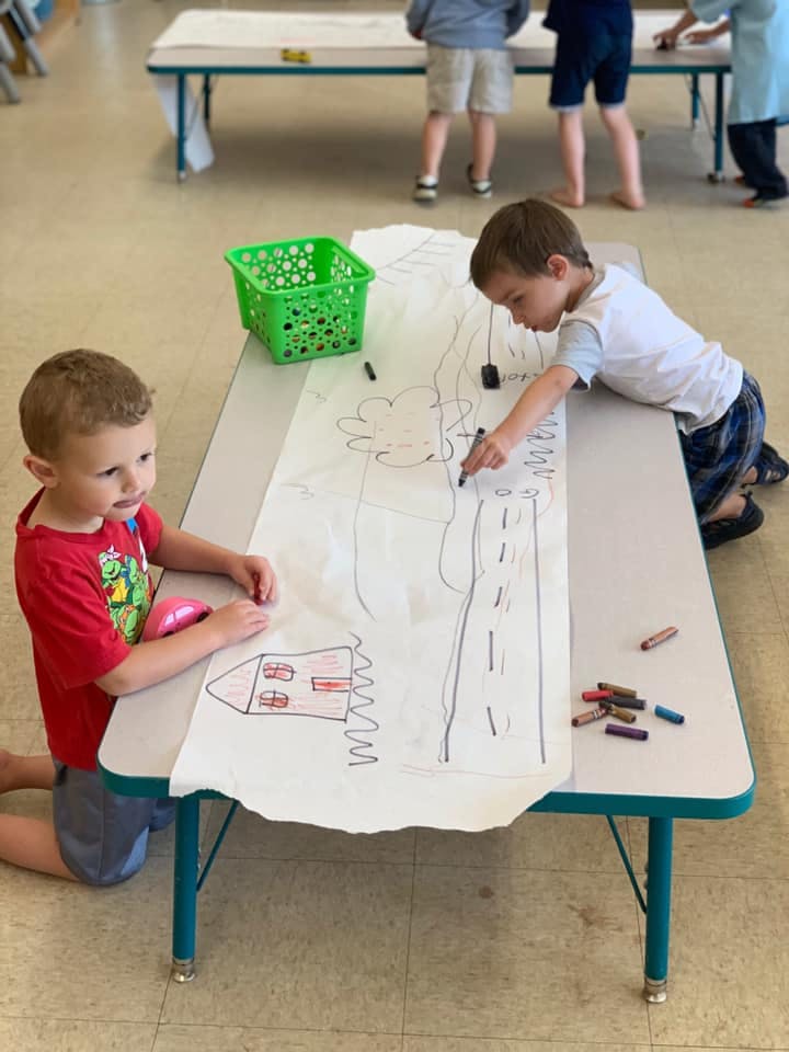 Two children drawing on a long sheet of paper on a table