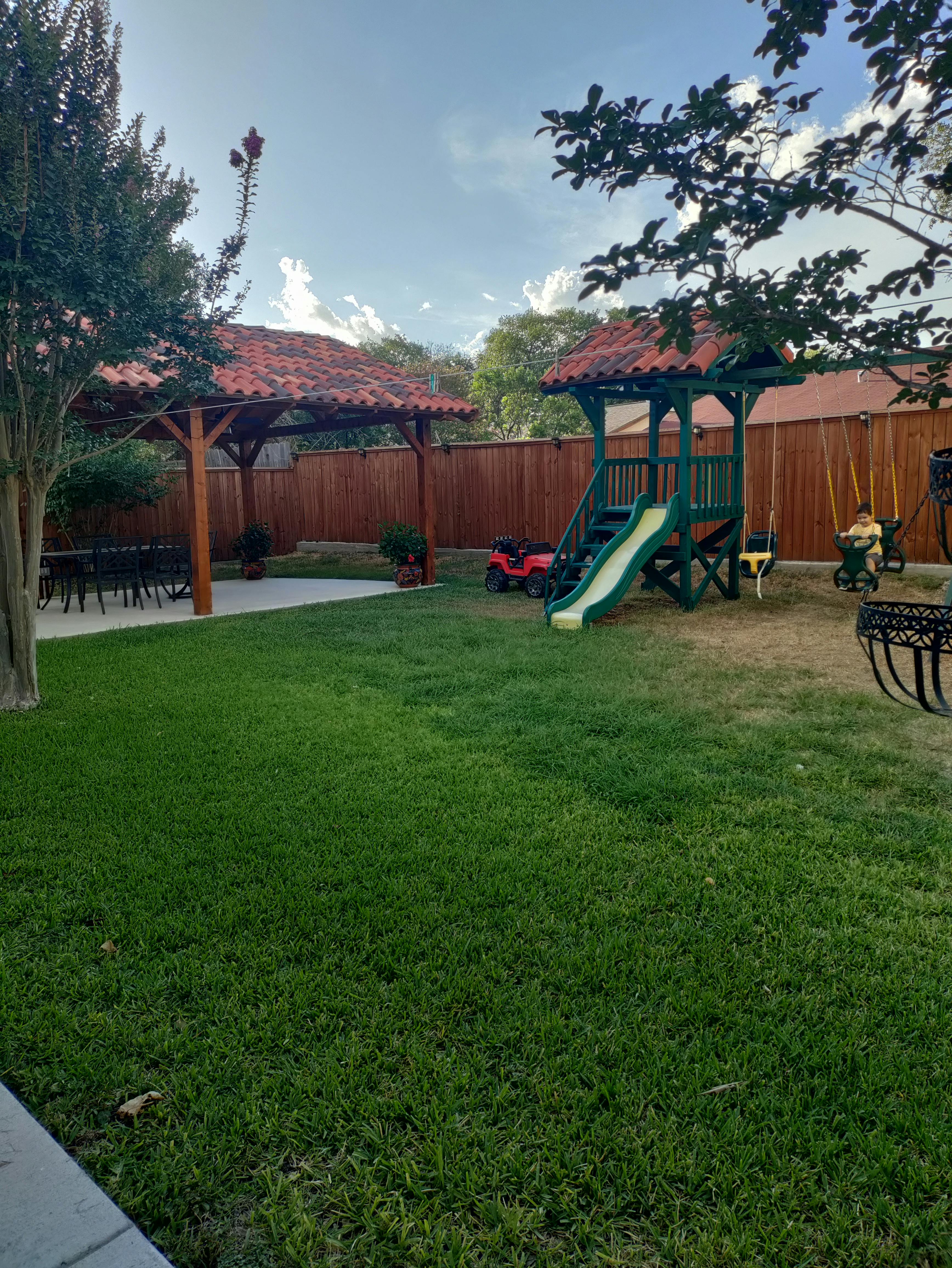 Backyard with a covered patio, green lawn, and a playset with a slide and swings