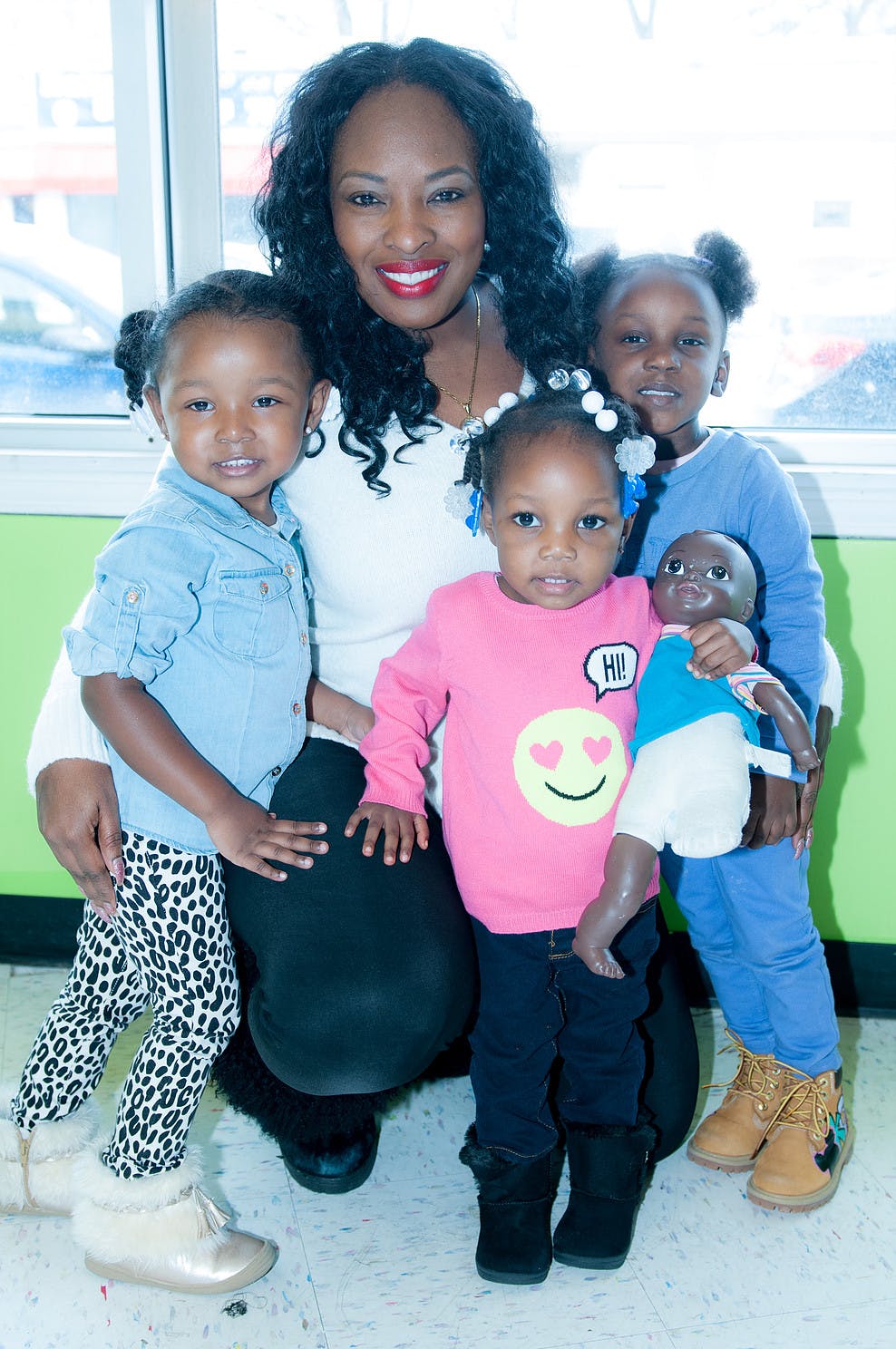 Person kneeling with three children, one holding a doll