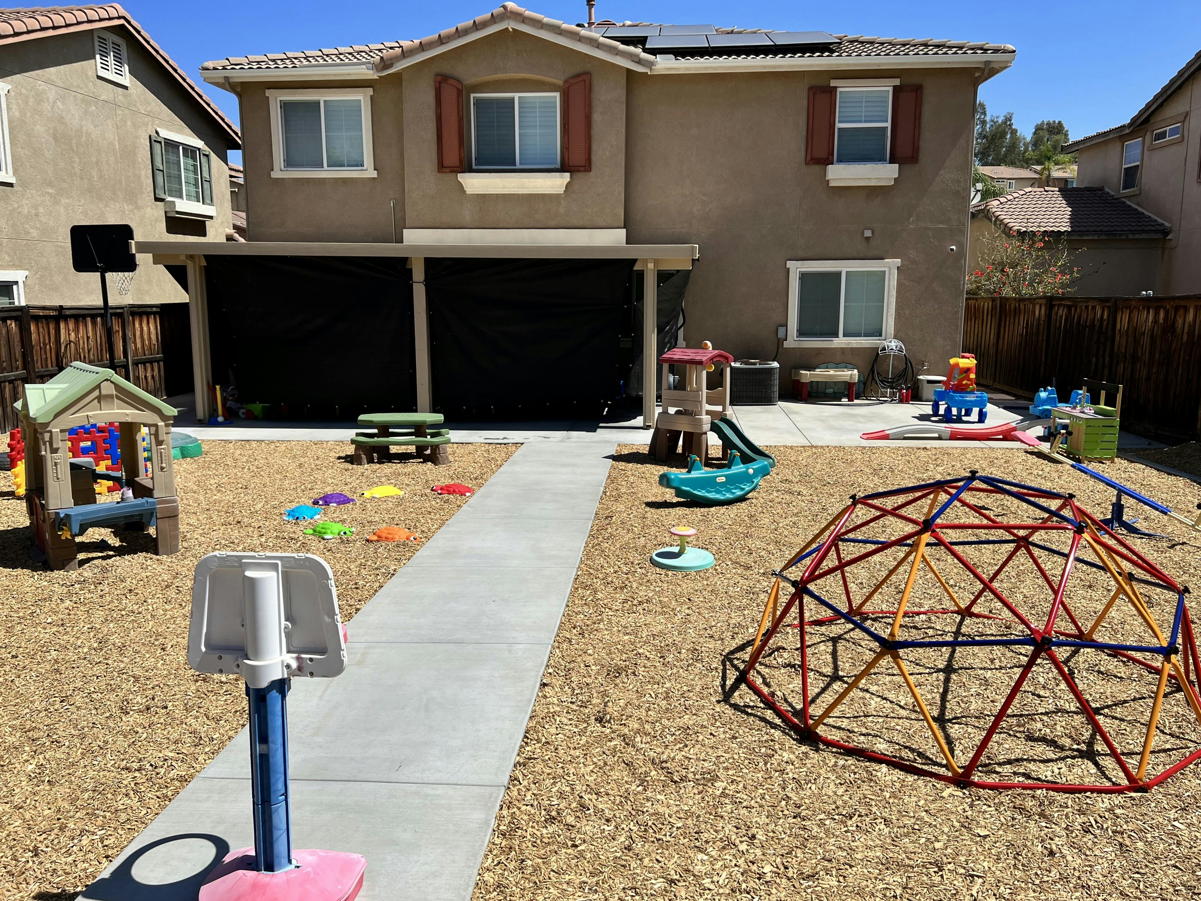 Backyard filled with children's play equipment, including a climbing dome and playhouse