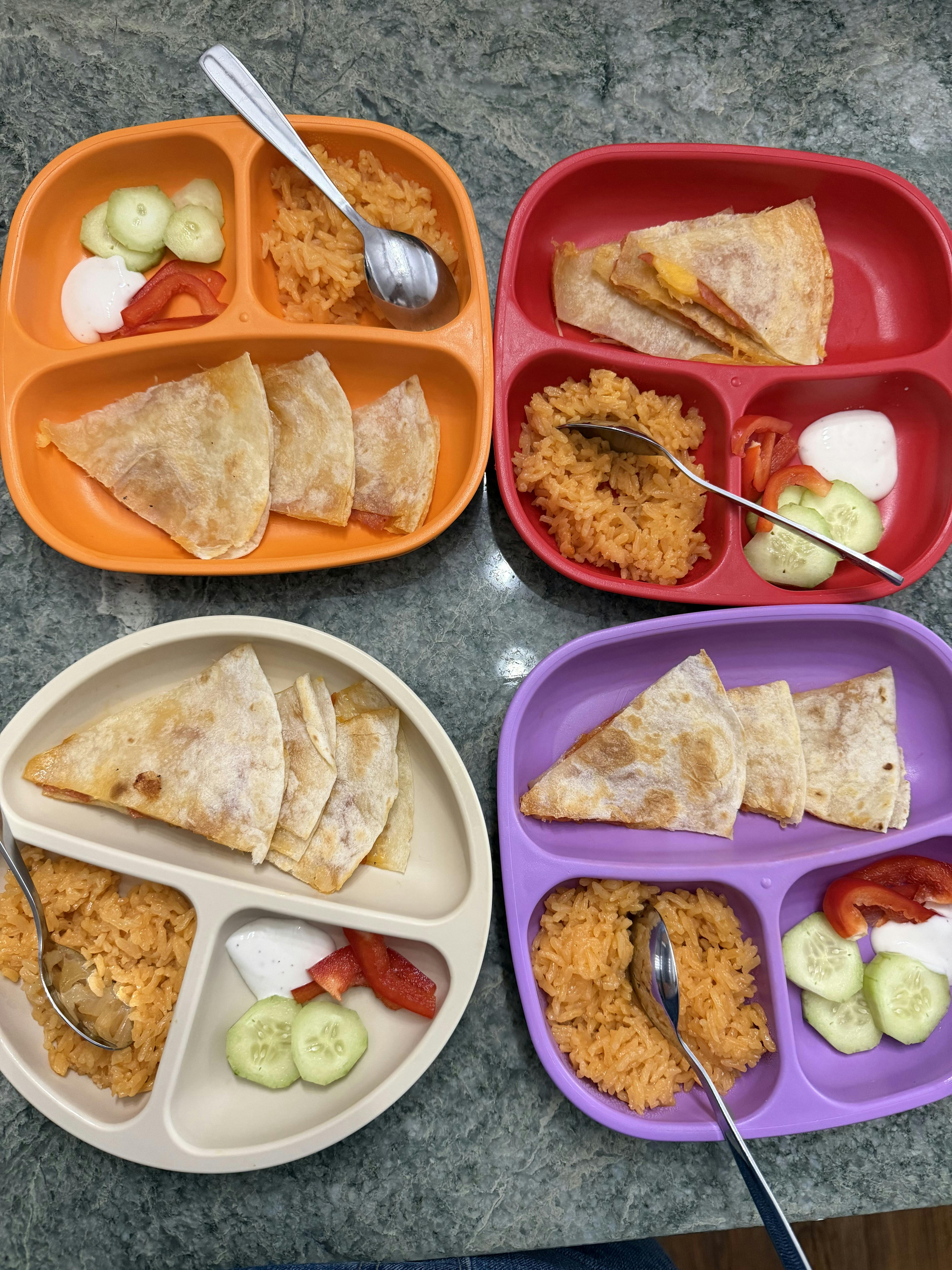Four children's plates with quesadillas, rice, cucumbers, red peppers, and dip