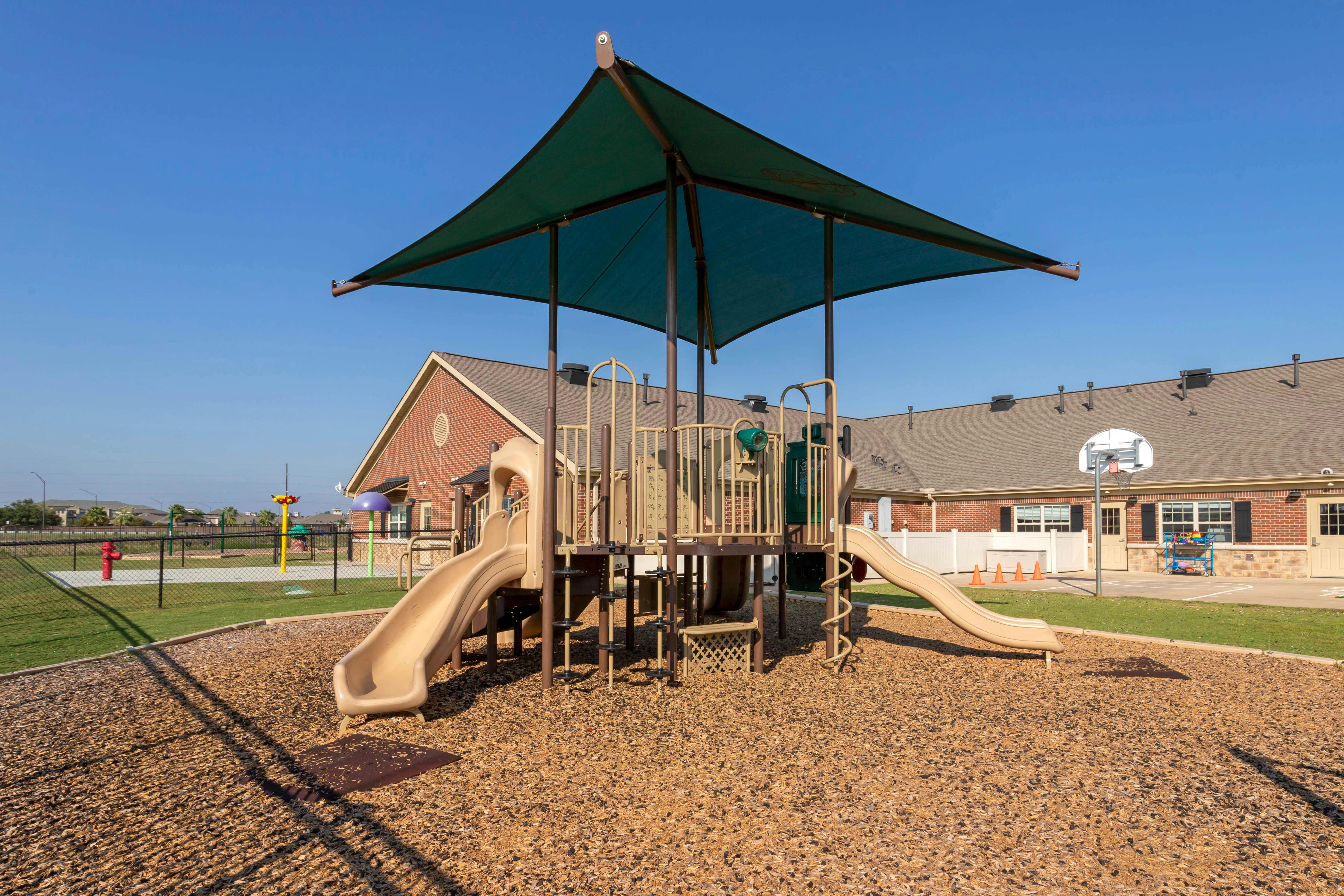 Playground with tan slides and climbing structures on wood chips, blue sky overhead