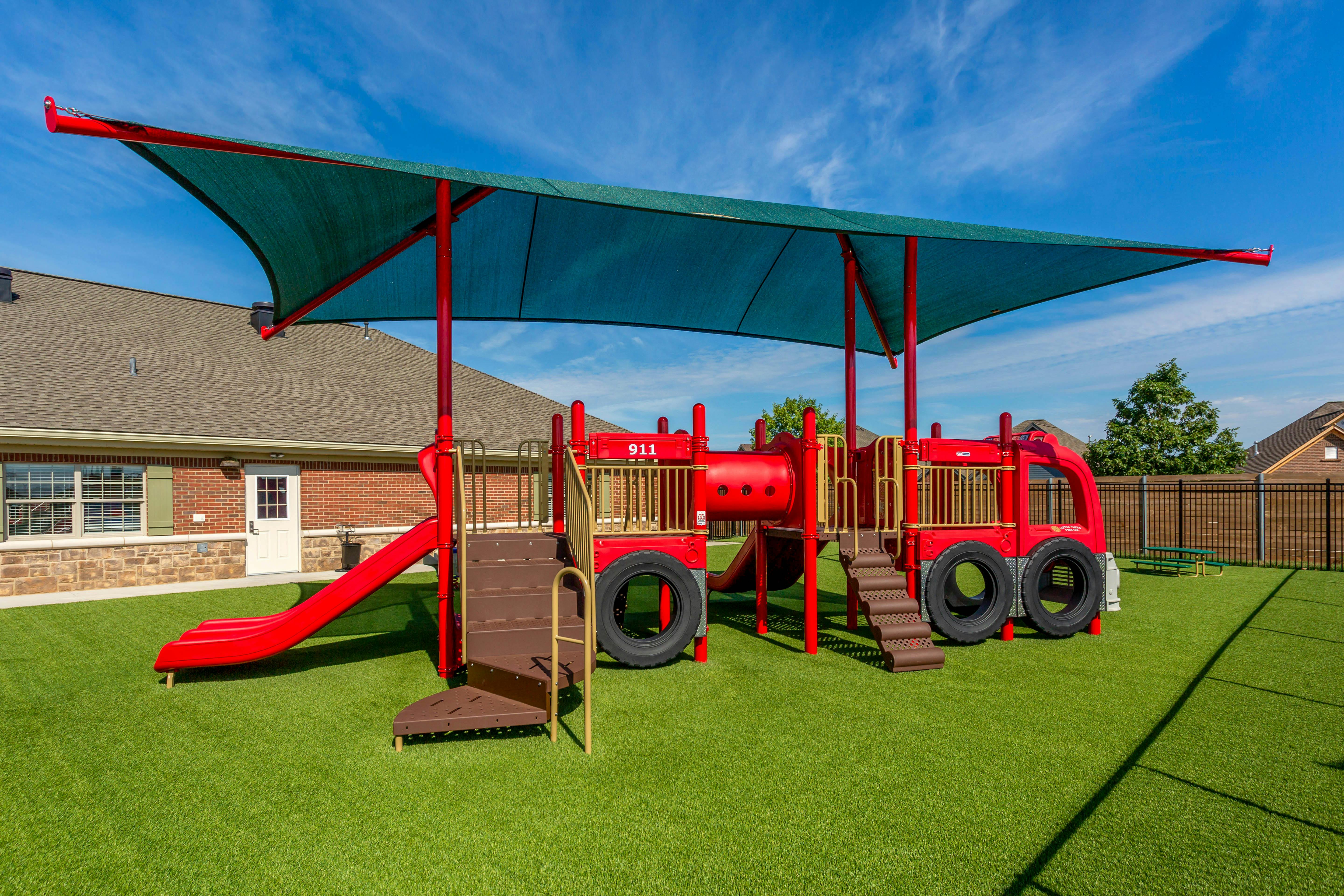 Red fire truck-shaped playground with slides and stairs under a shade canopy