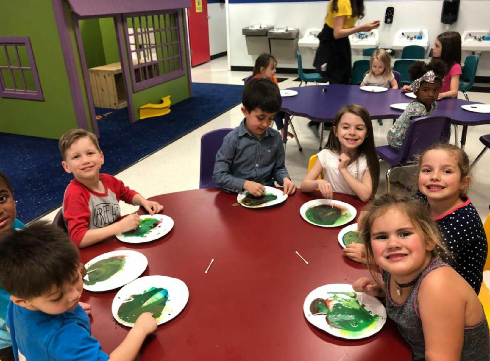 Children sitting at tables with plates of green paint