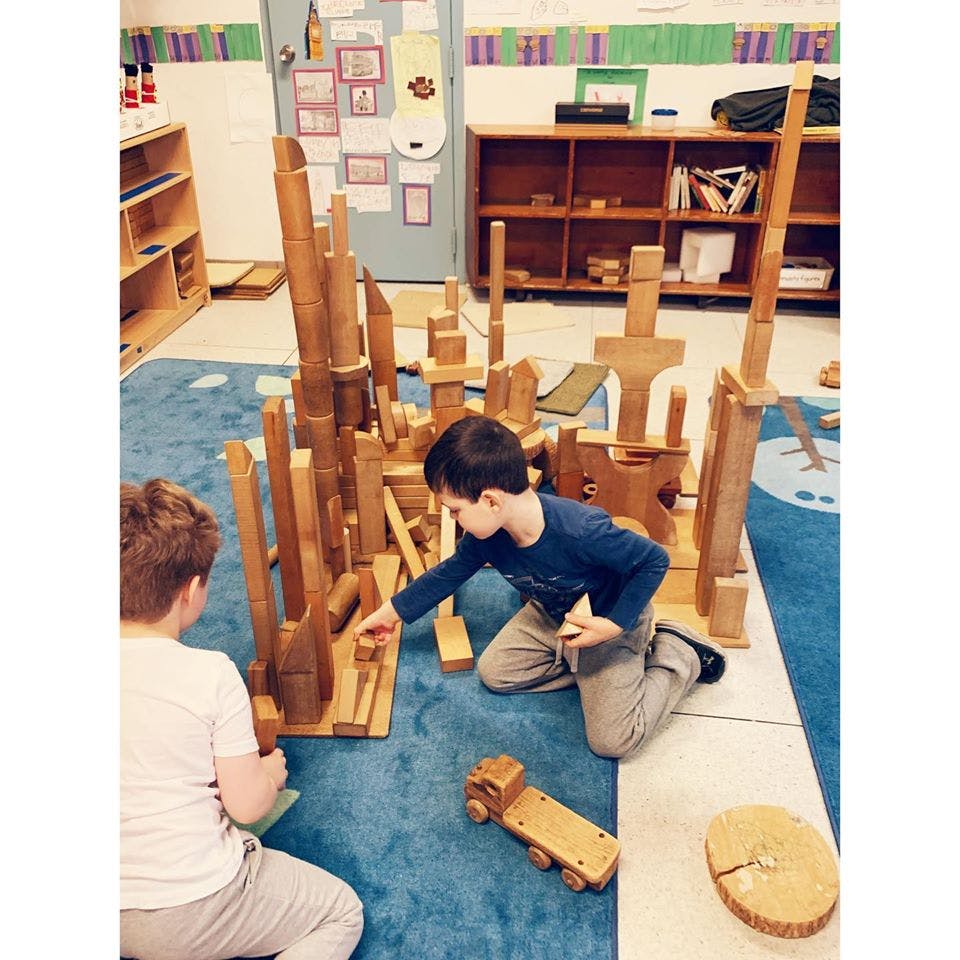 Two children playing with wooden blocks on a blue rug in a classroom