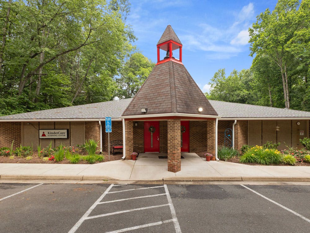 A low-rise building with a brick facade and a steeple-like roof in front of trees