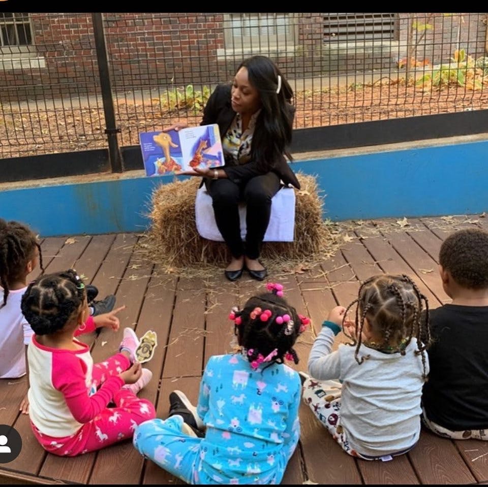 Person reading a book to a group of children sitting on the ground