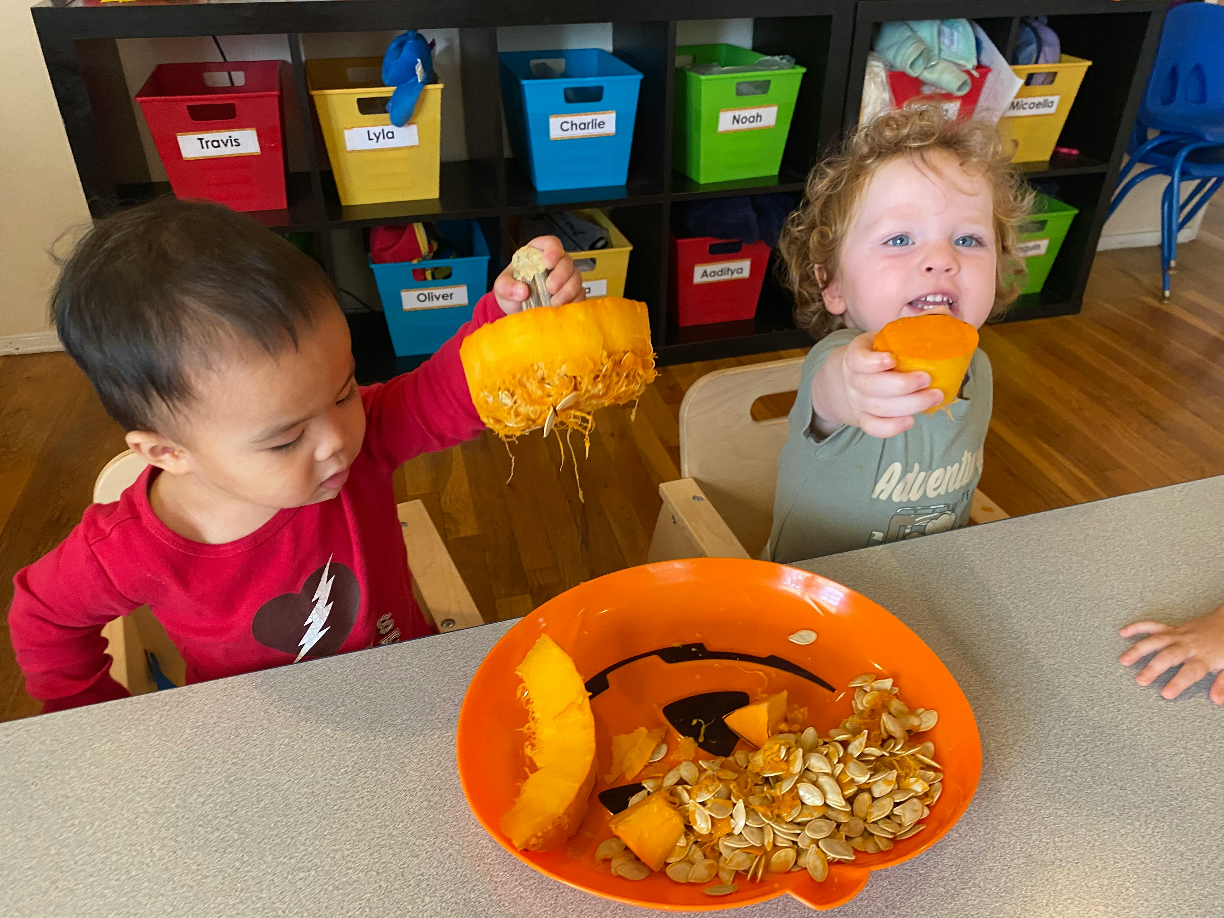 Two children playing with pumpkin pieces and seeds at a table