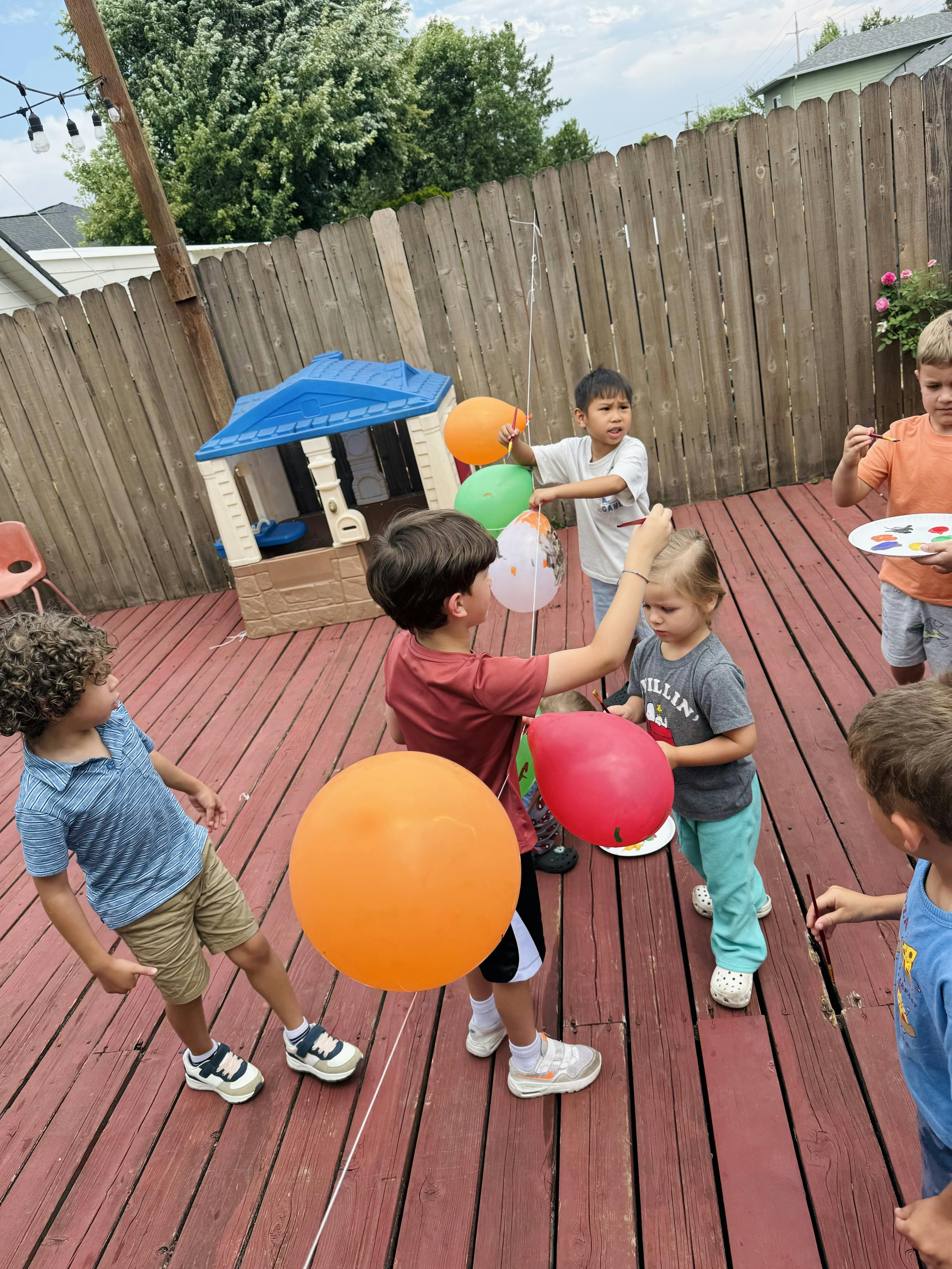 Children painting balloons on a wooden deck