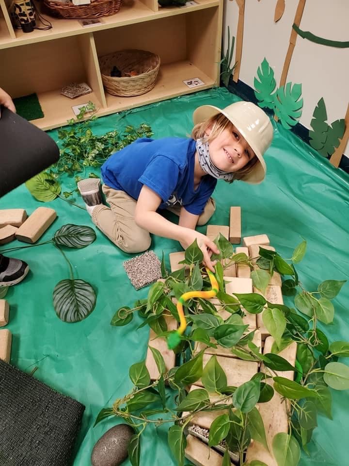 Child in a safari hat playing with blocks and artificial plants