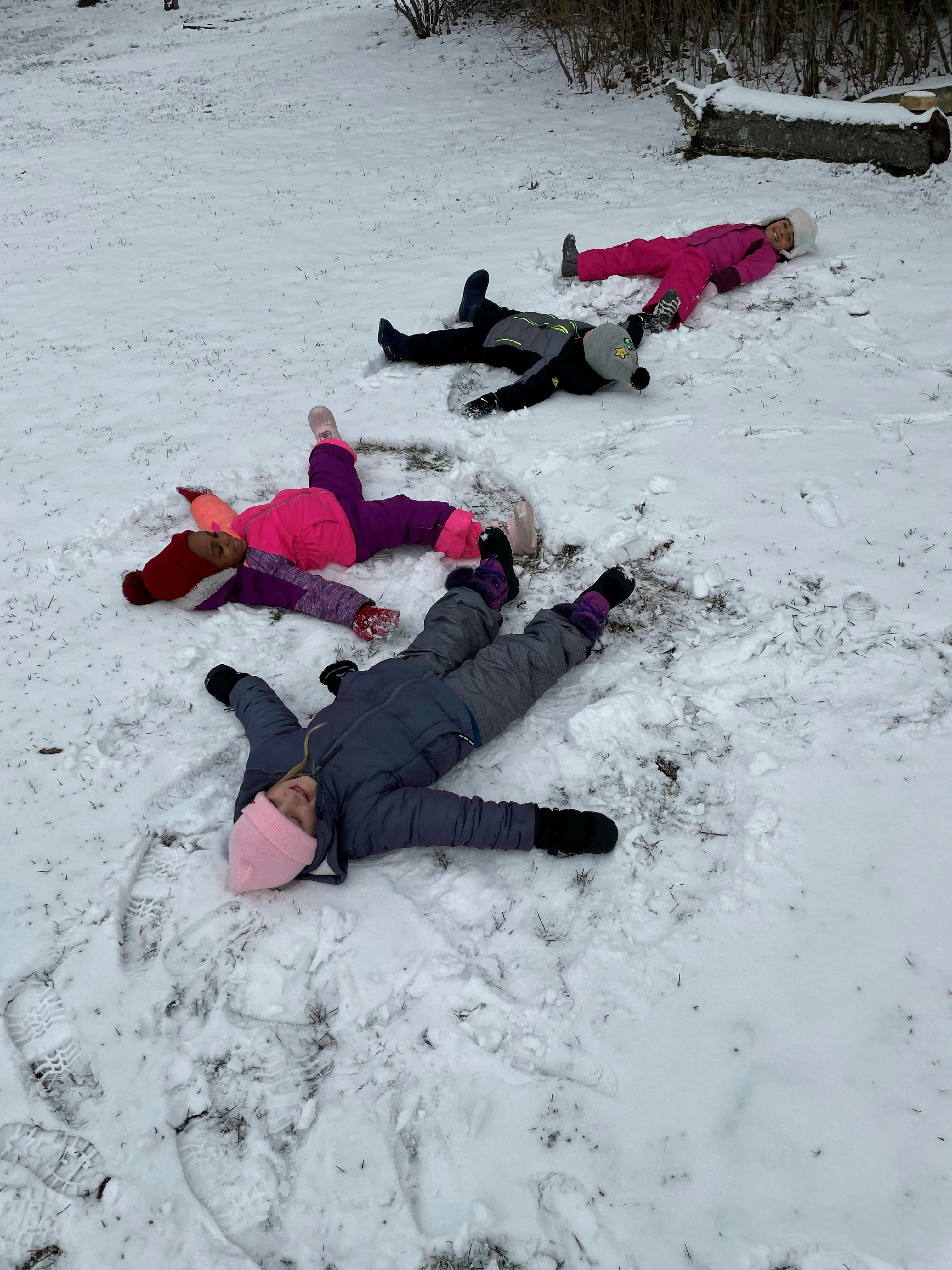 Four children lying in the snow making snow angels