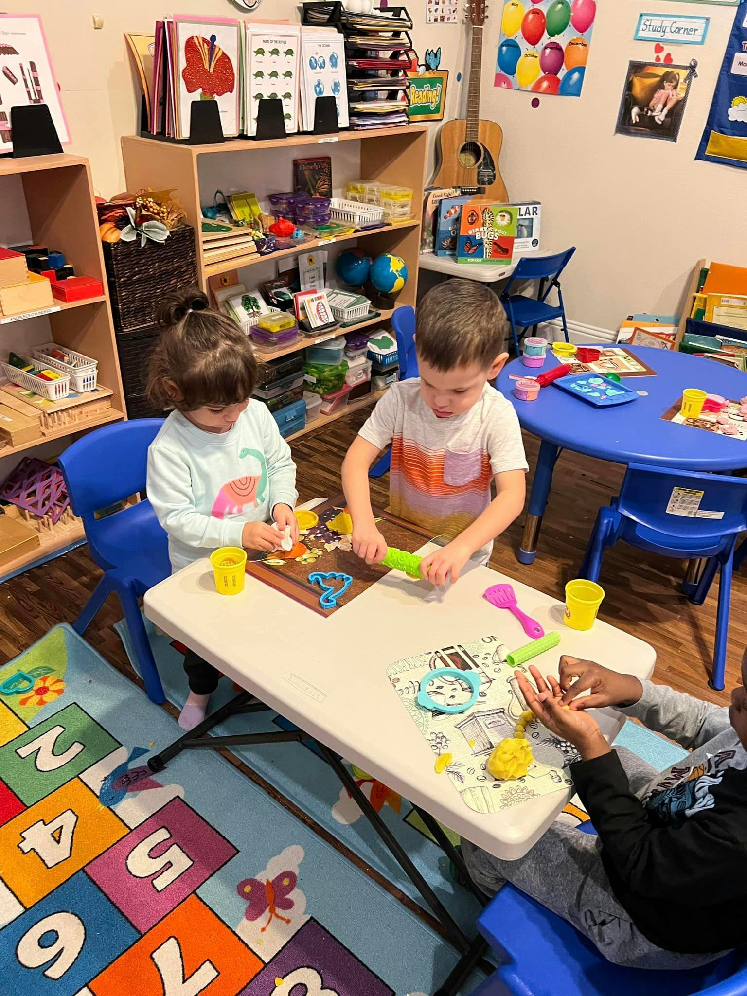 Three children playing with modeling clay at a table in a classroom
