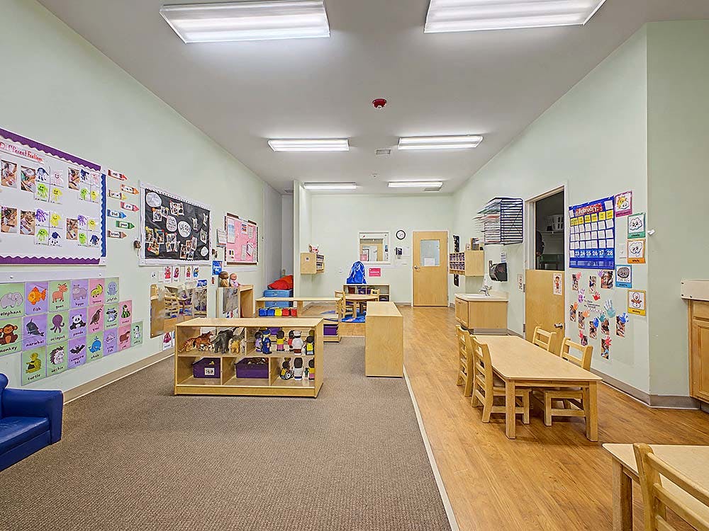 Empty preschool classroom with bulletin boards, small tables, and shelves of toys