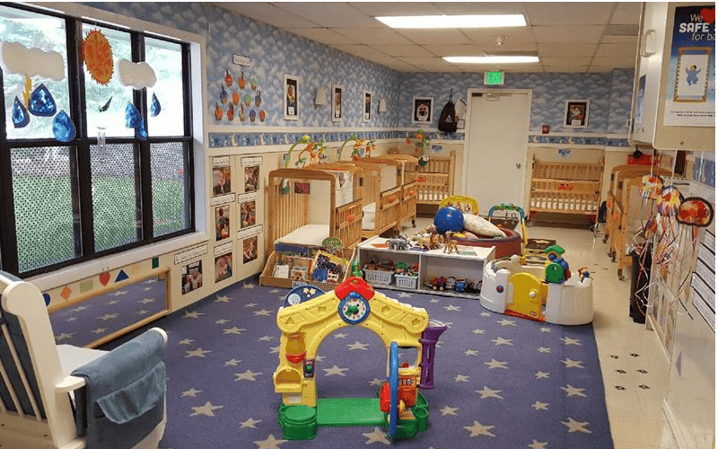 Cribs and toys in a daycare room with a star-patterned rug
