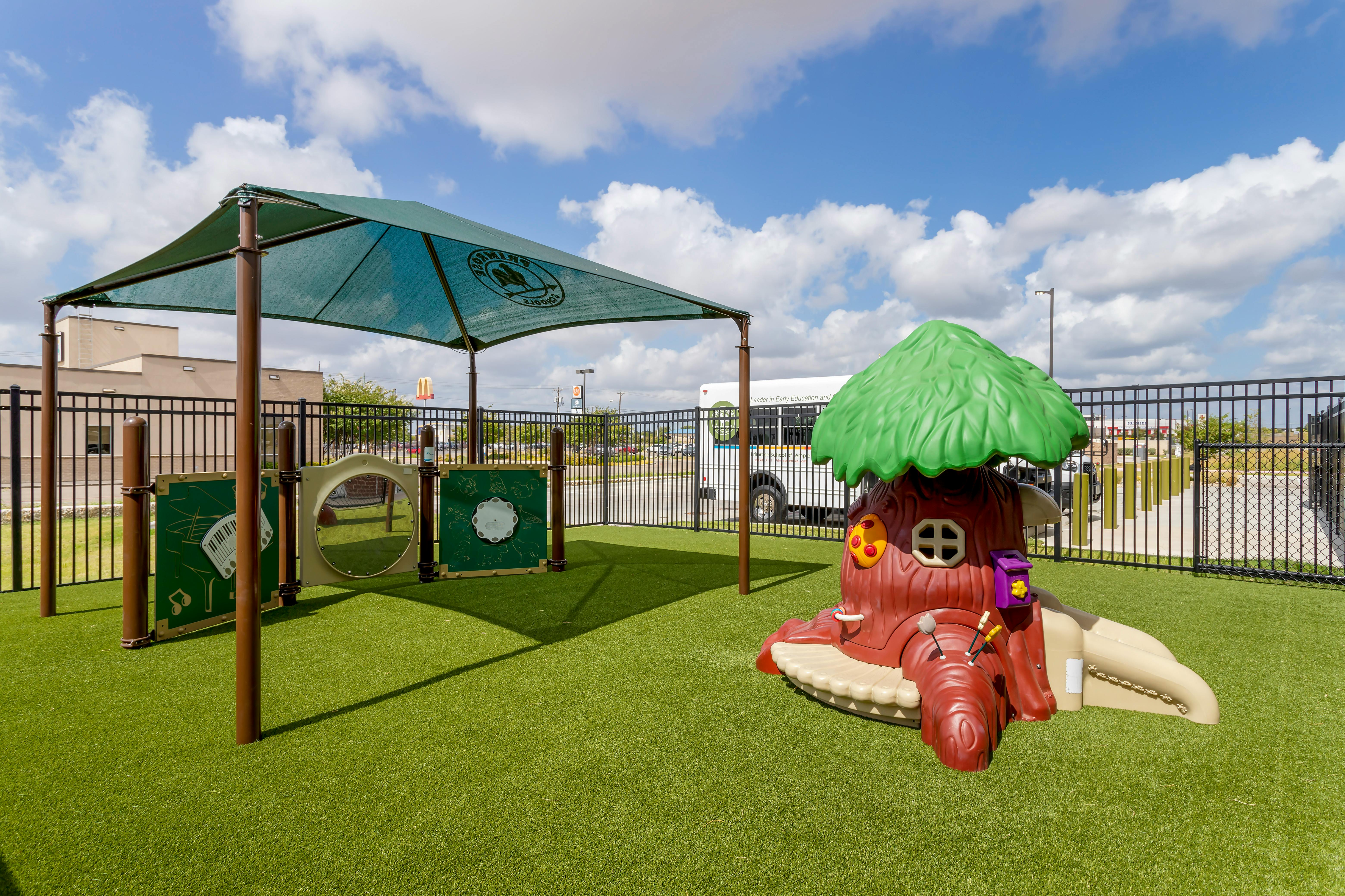 Playground area with artificial turf, a green shade, and a tree-shaped play structure