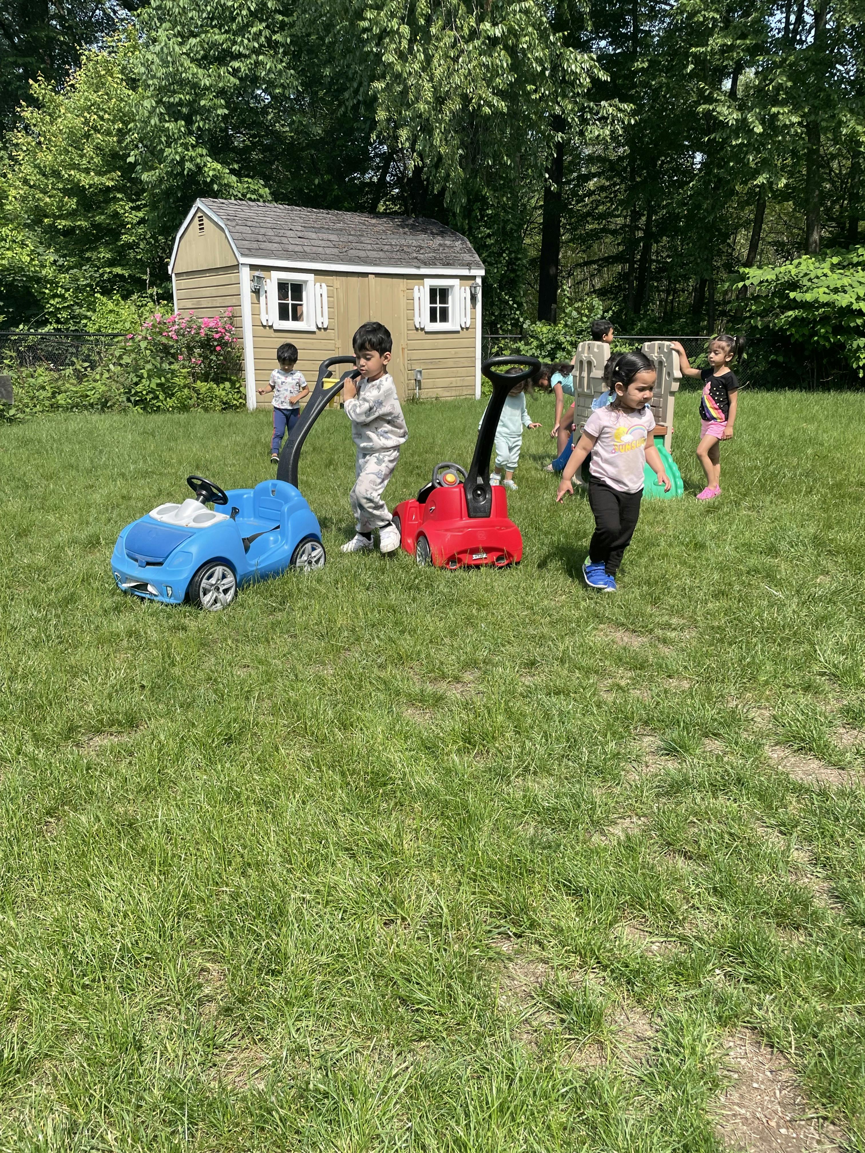 Children playing with toy cars and lawnmowers in a grassy yard