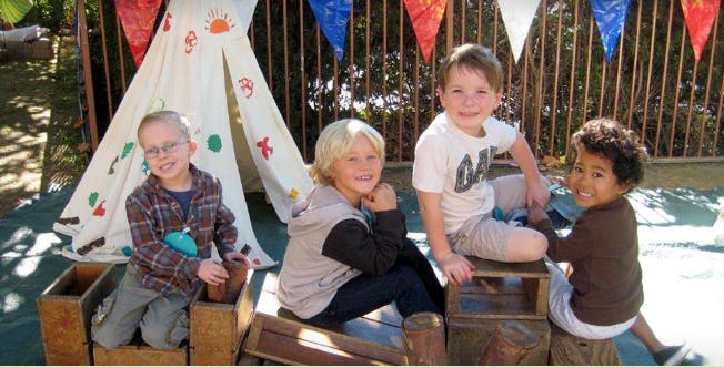 Four children sitting in front of a teepee
