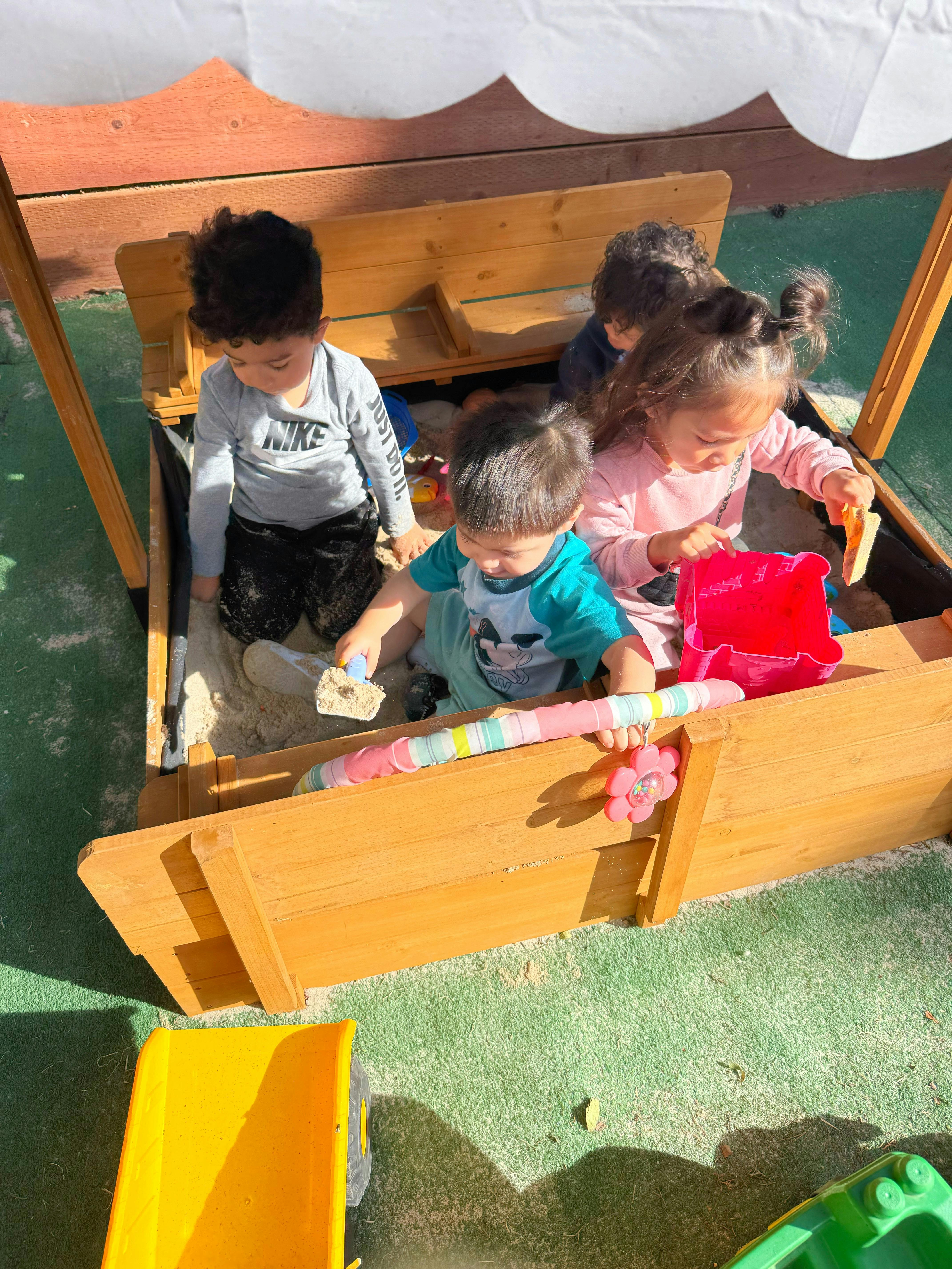 Children playing with sand in a wooden sandbox