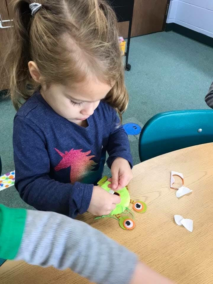 Child playing with a green craft toy at a table