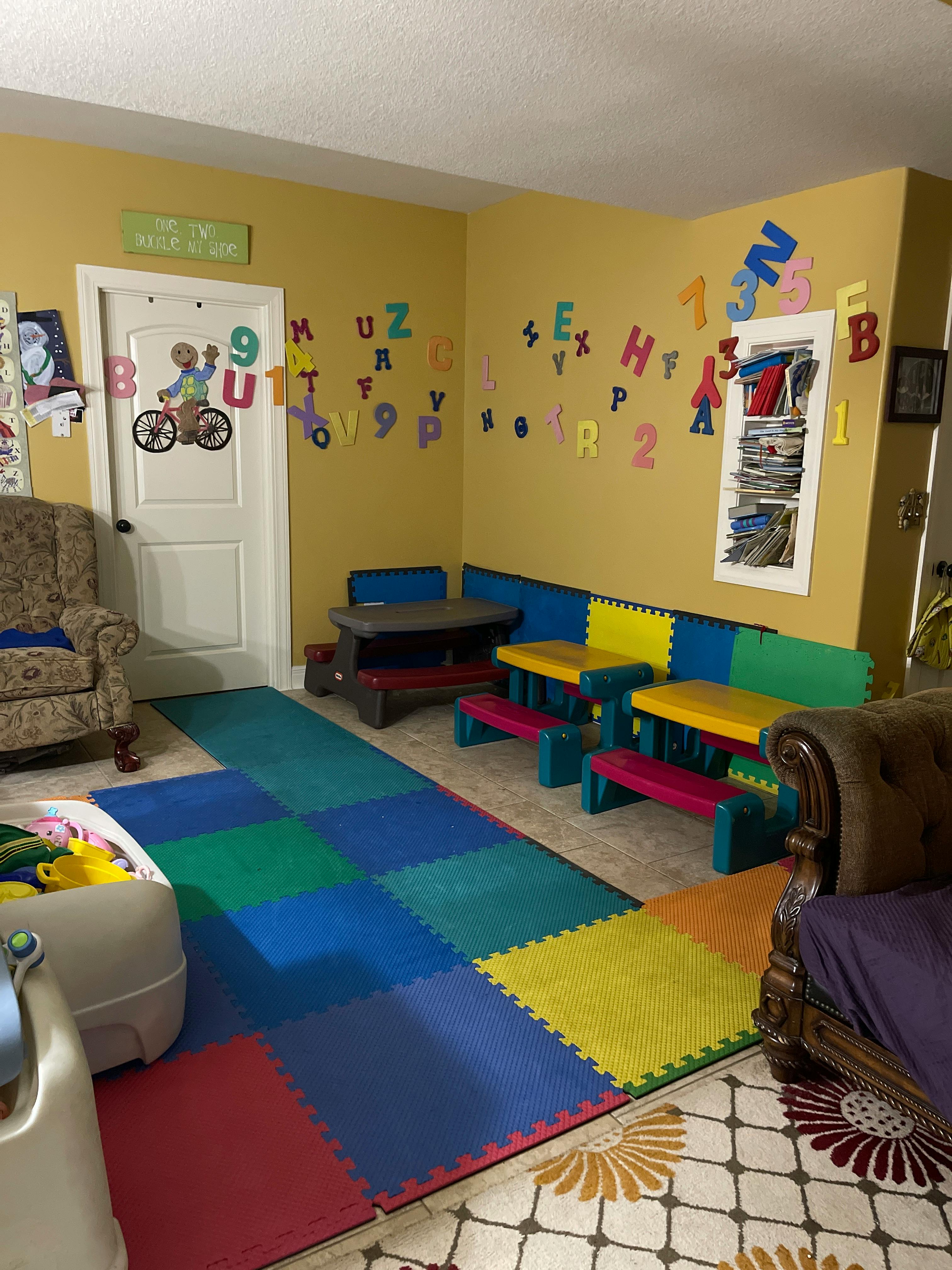 Playroom with colorful floor mats, small tables, and alphabet letters on the wall
