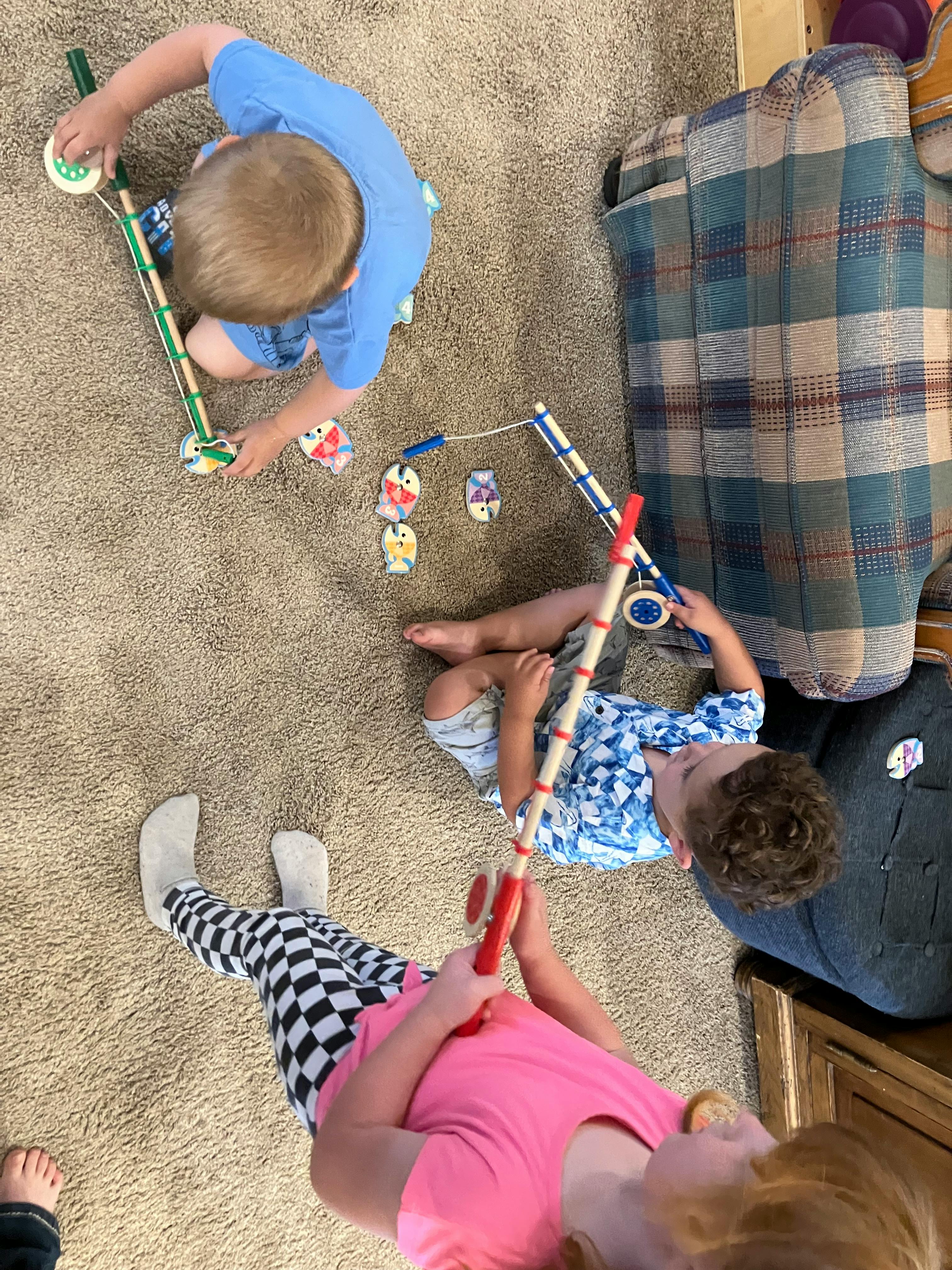 Three children playing with toy fishing rods on a carpet