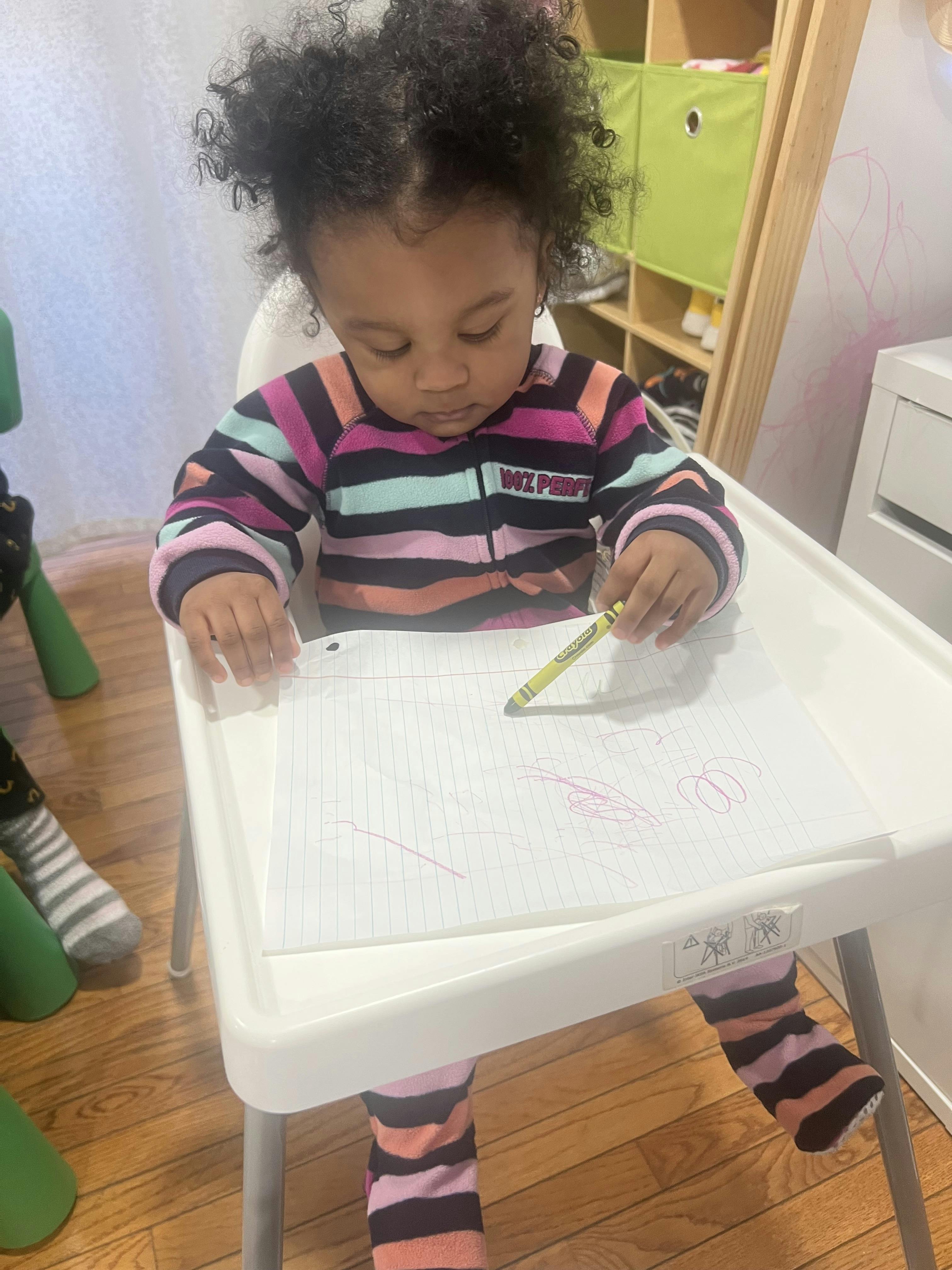 Child drawing on paper with a crayon in a high chair