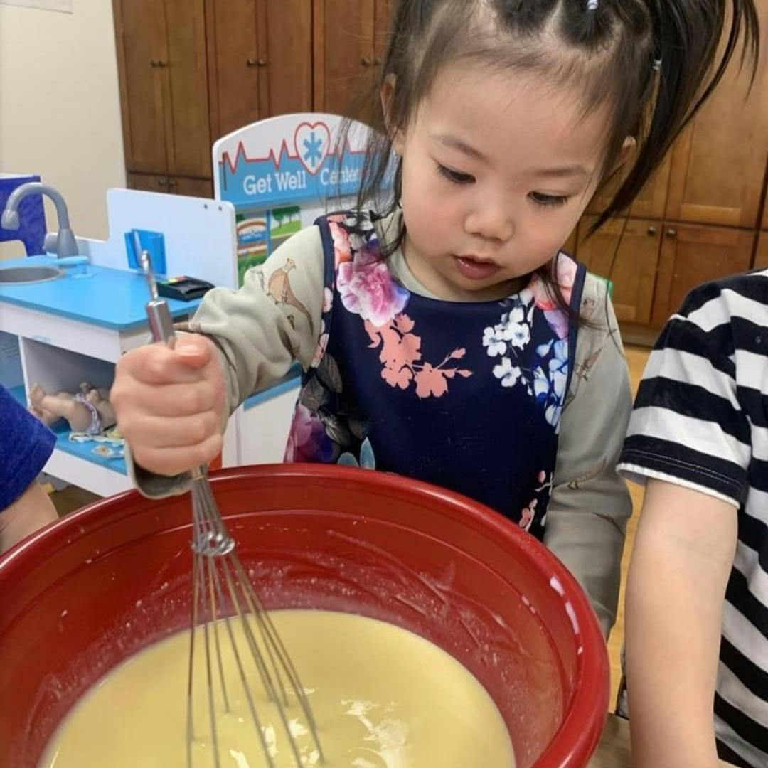 Child whisking liquid in a red bowl