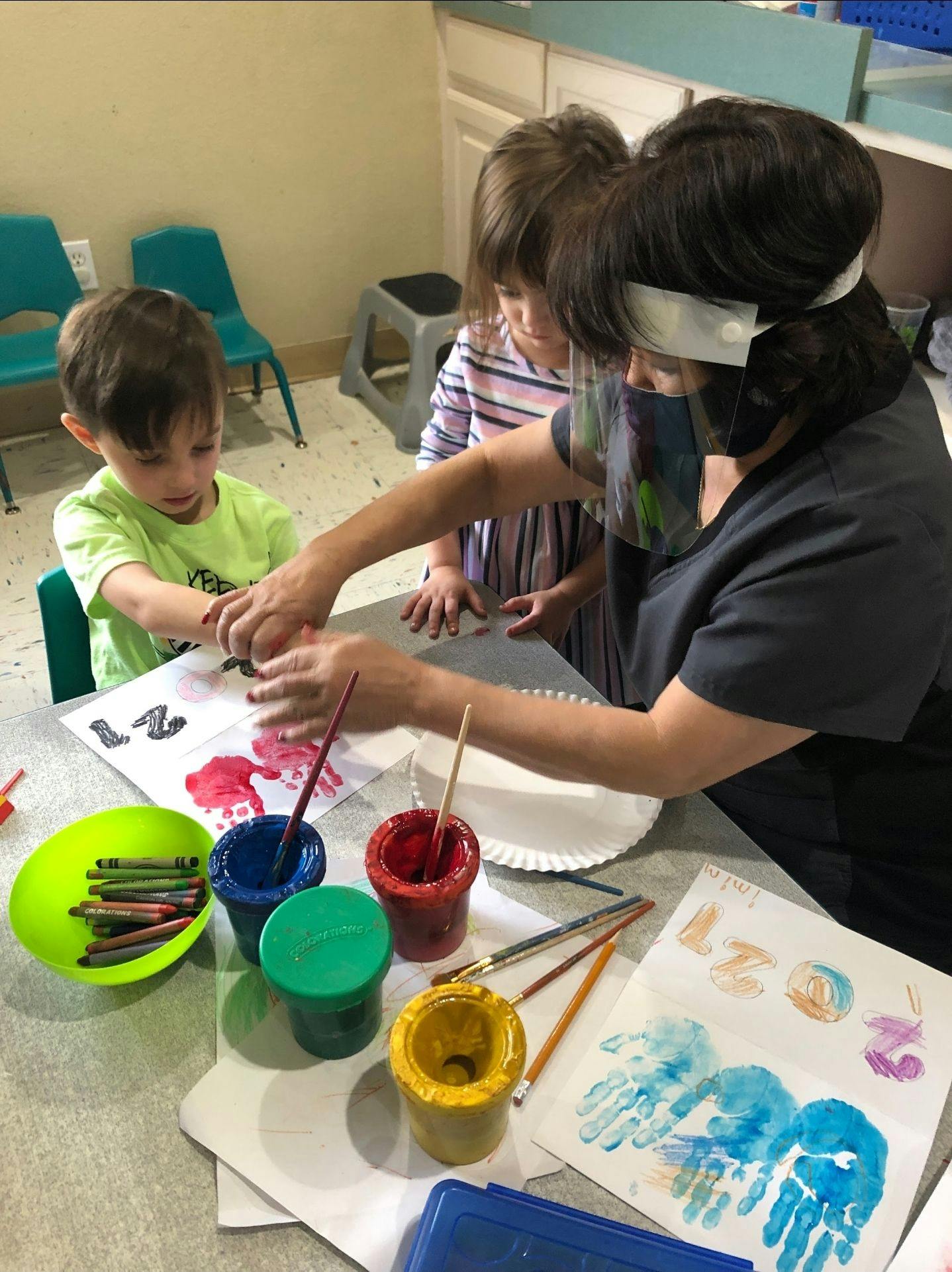 Adult and two children painting with hands at a table