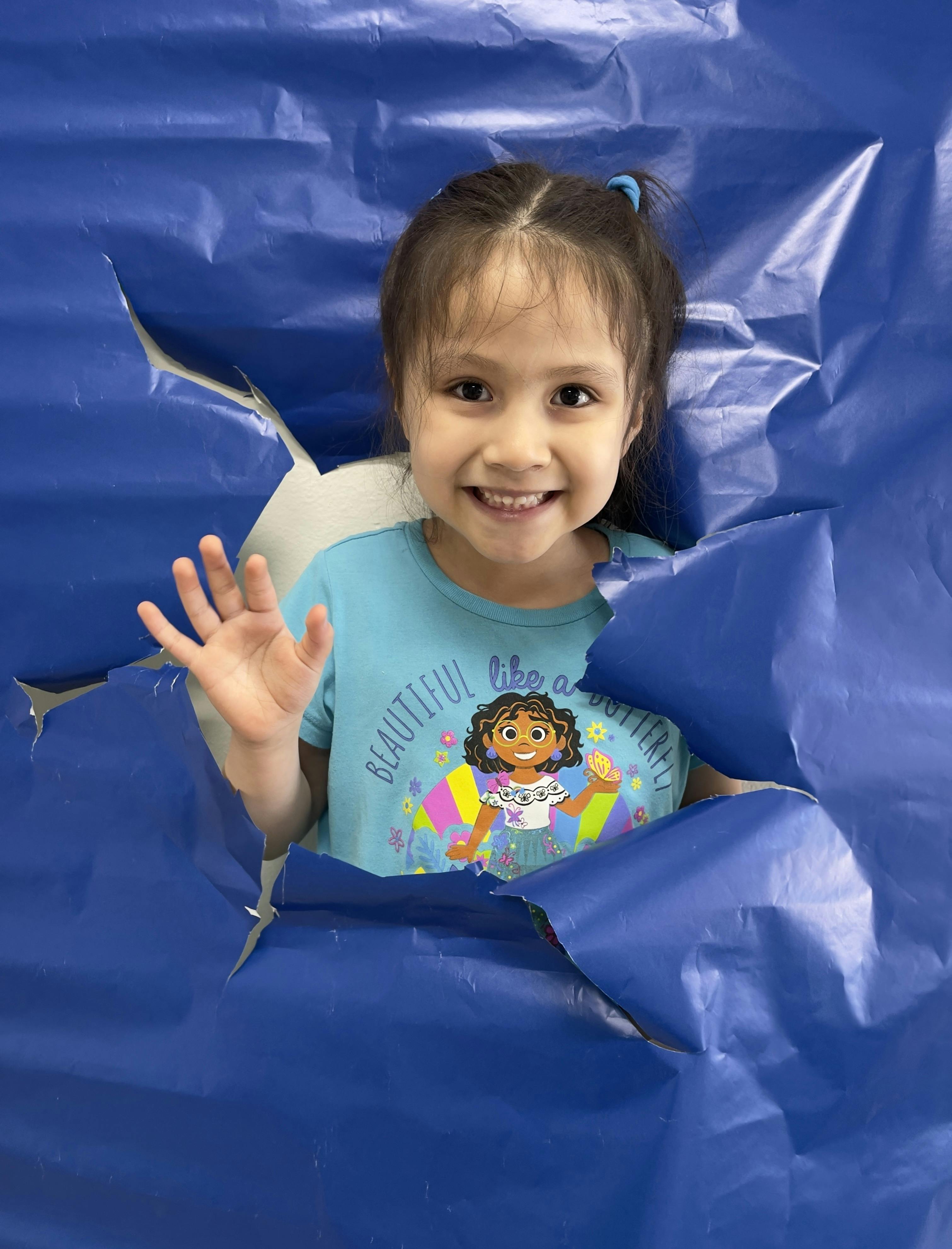 Child looking through a torn blue sheet
