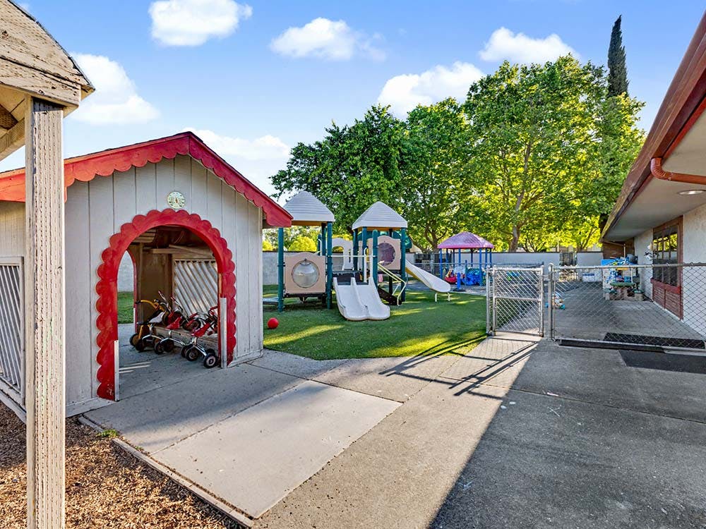 A playground with a small shed and tricycles, and a slide set with swings