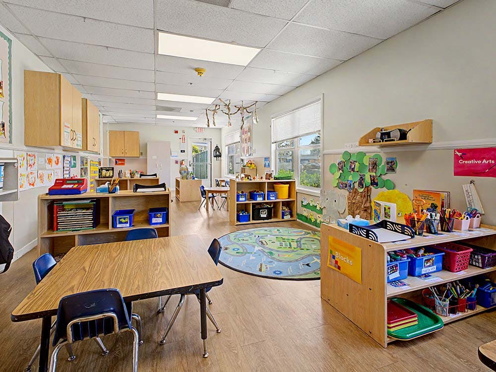 Classroom with tables, chairs, shelves of supplies, and windows