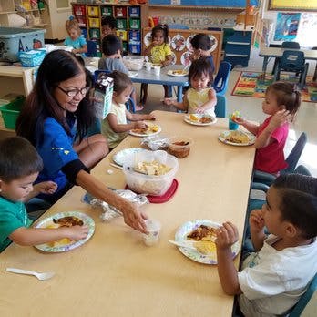Adult serving food to children at a table in a classroom