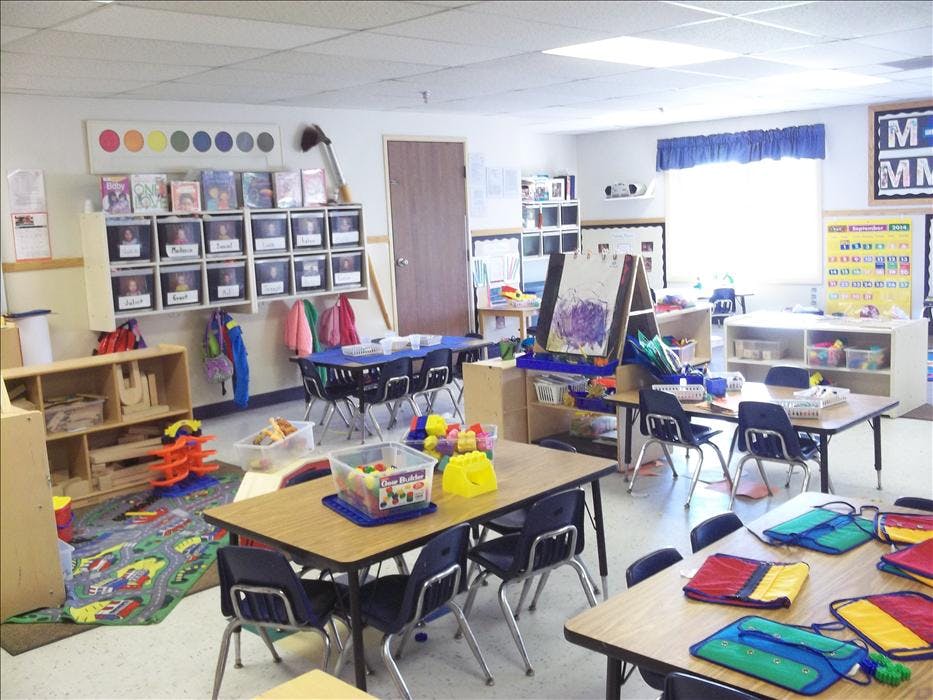 Classroom with small tables and chairs, toys, and an easel with a painting