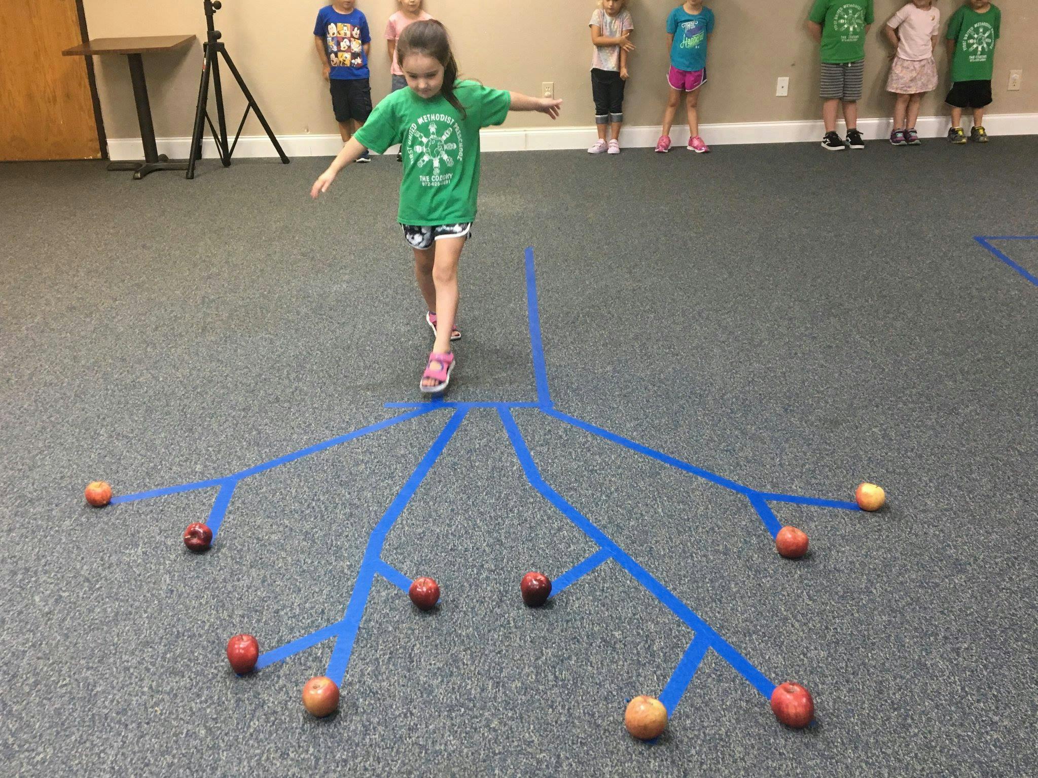 Child balancing on blue tape lines on the floor with small balls