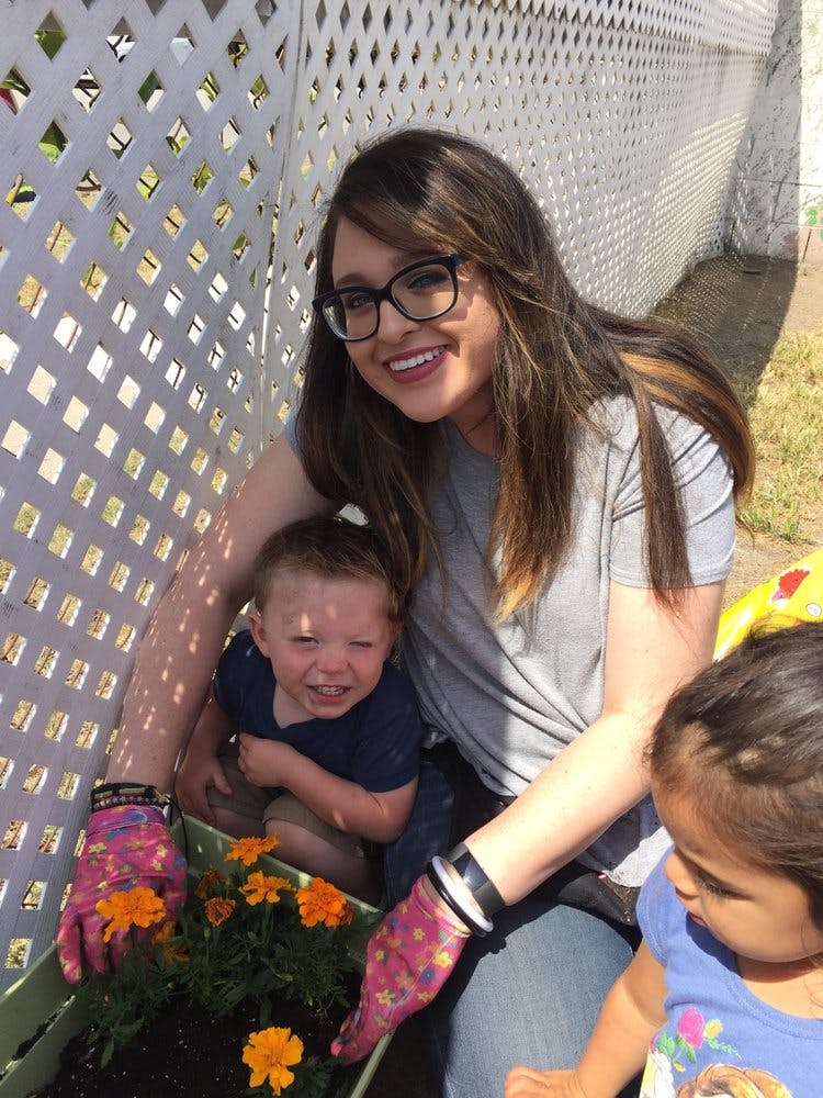 Person in glasses and two children planting flowers in a garden
