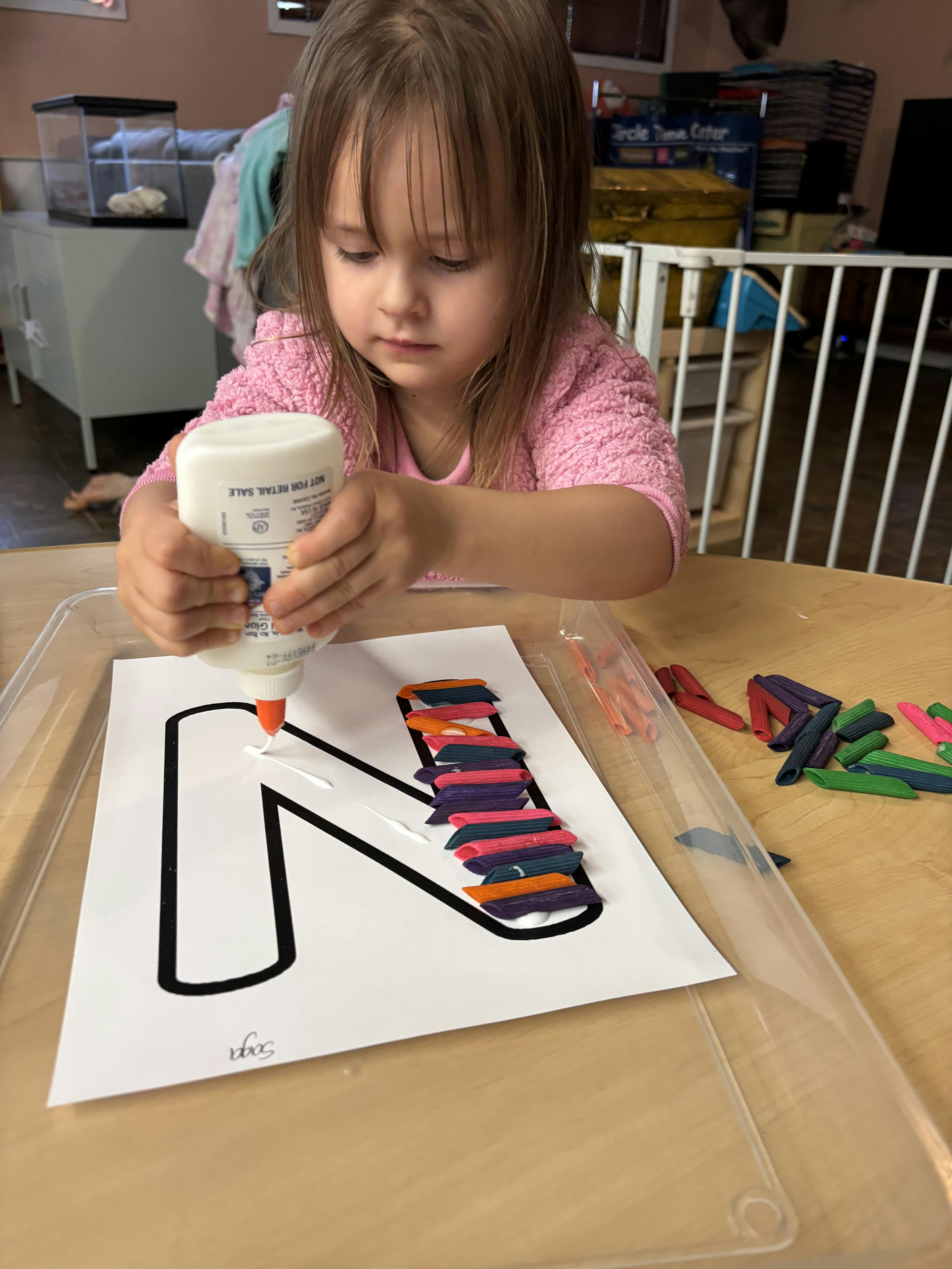 Child squeezing glue onto a paper with a letter N outline