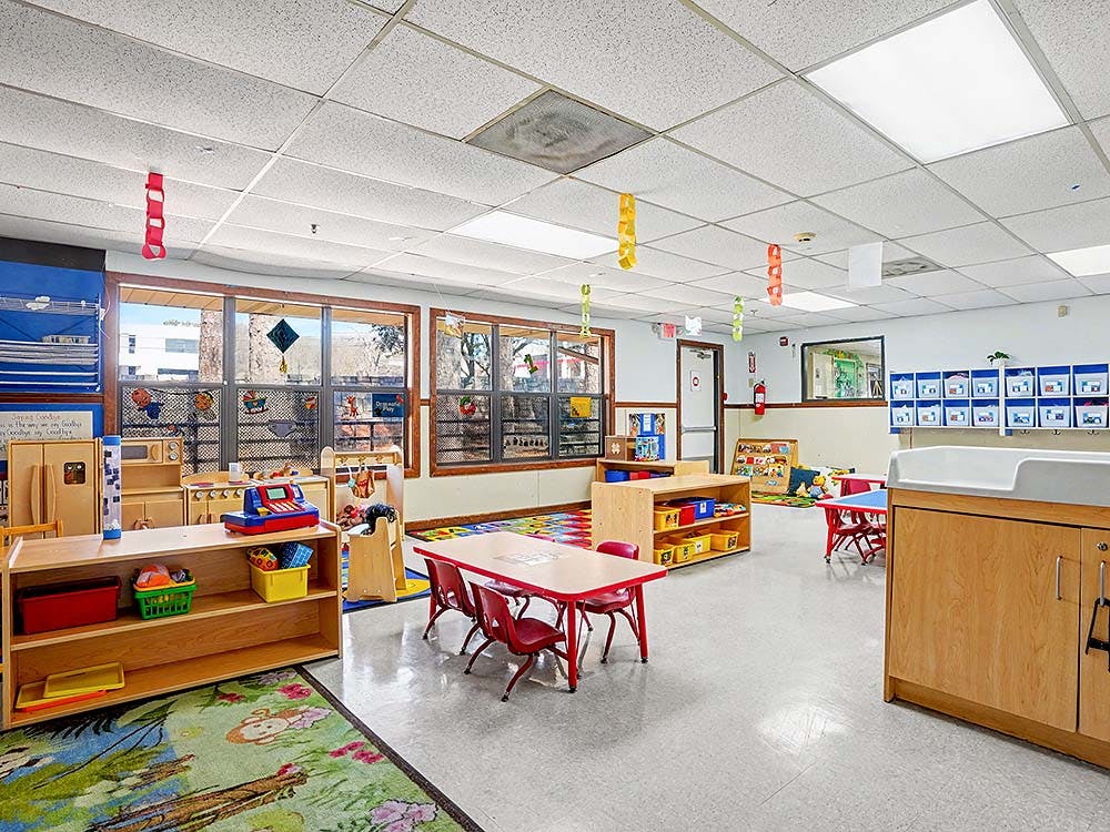 Classroom with small tables and chairs, play kitchen, and windows