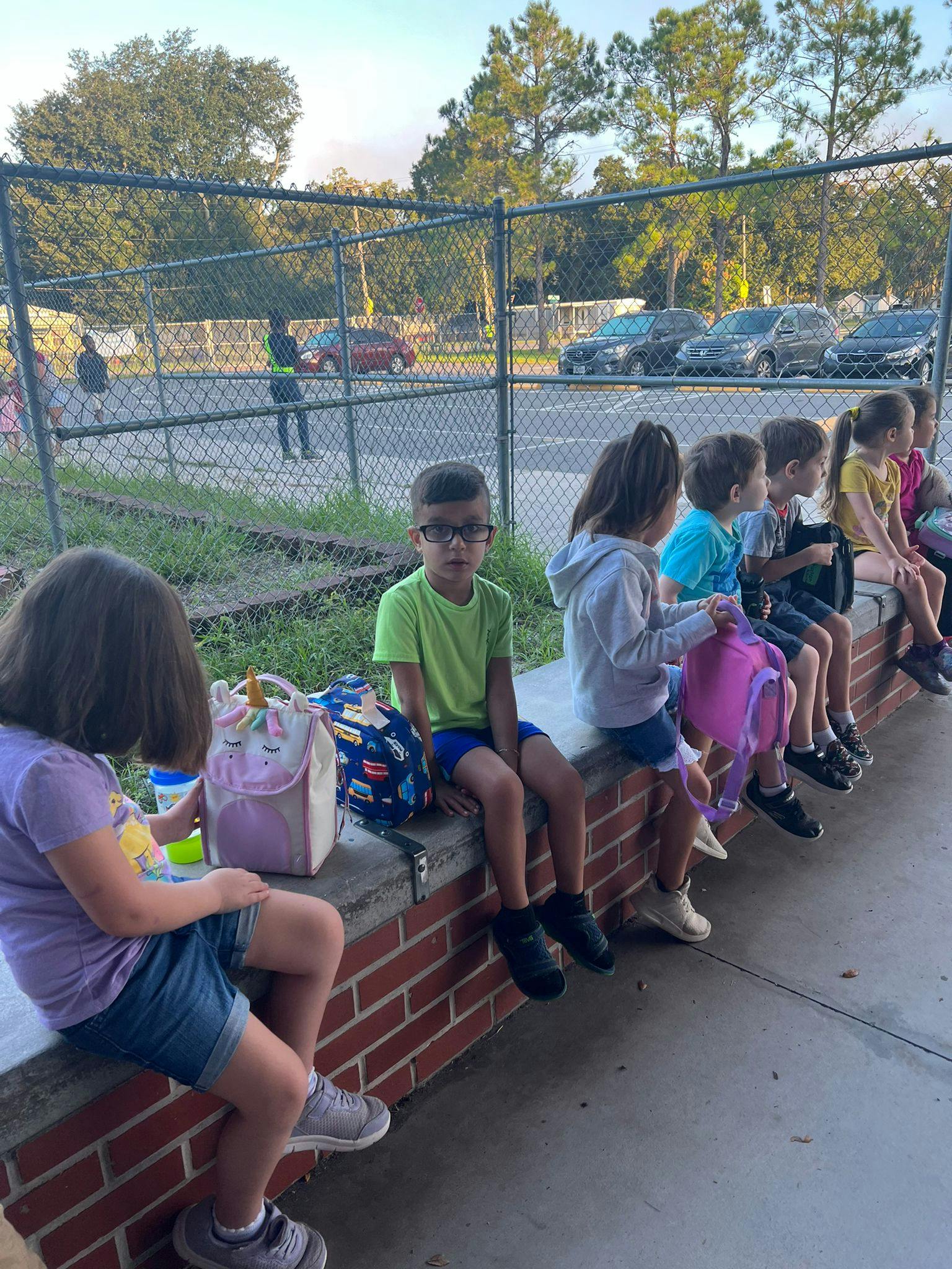 Children sitting on a brick ledge with backpacks