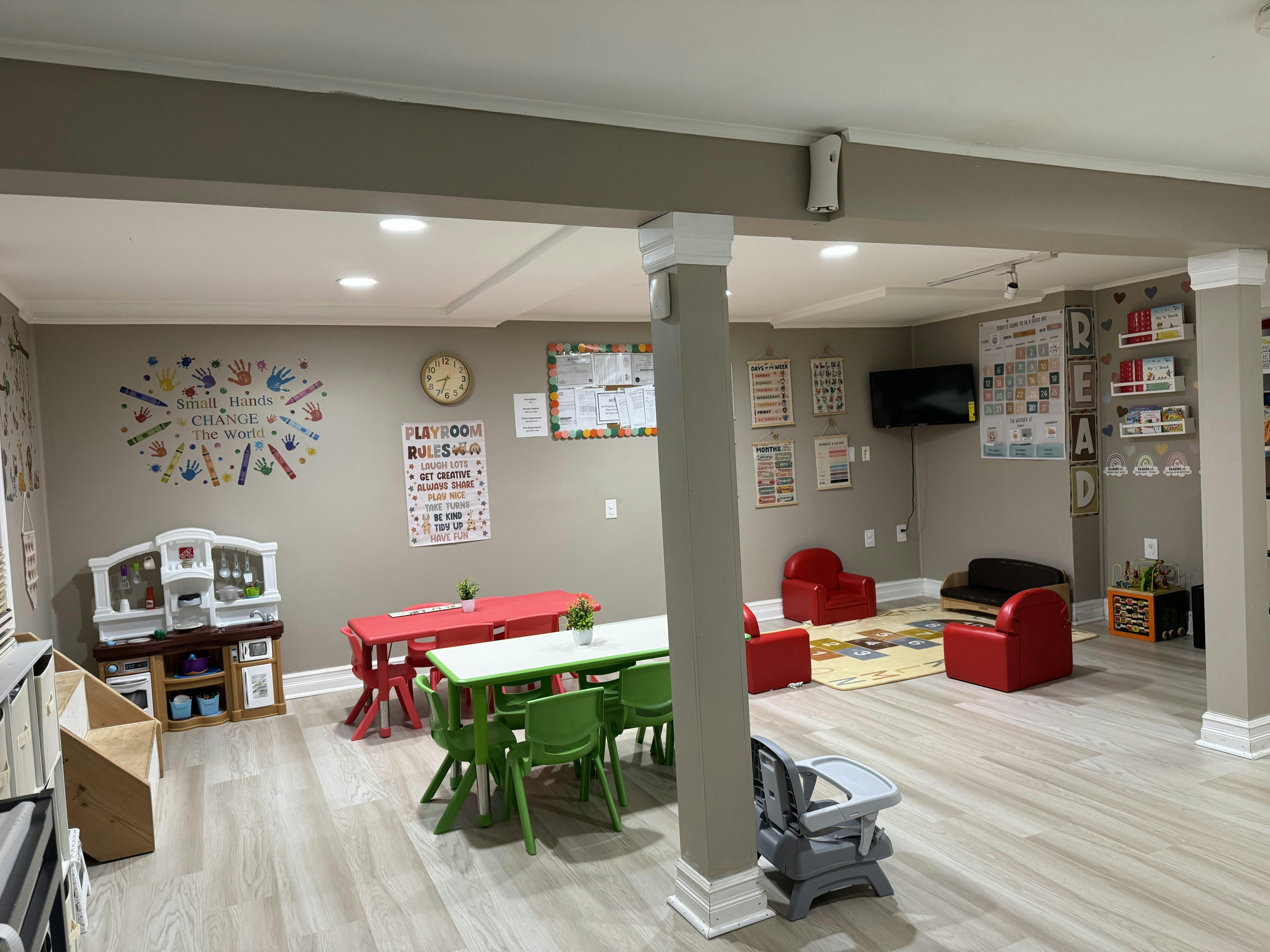A furnished child playroom with small tables, chairs, and educational wall decor