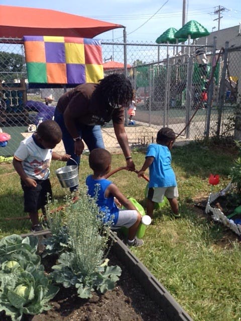 Adult and three children watering plants in a garden
