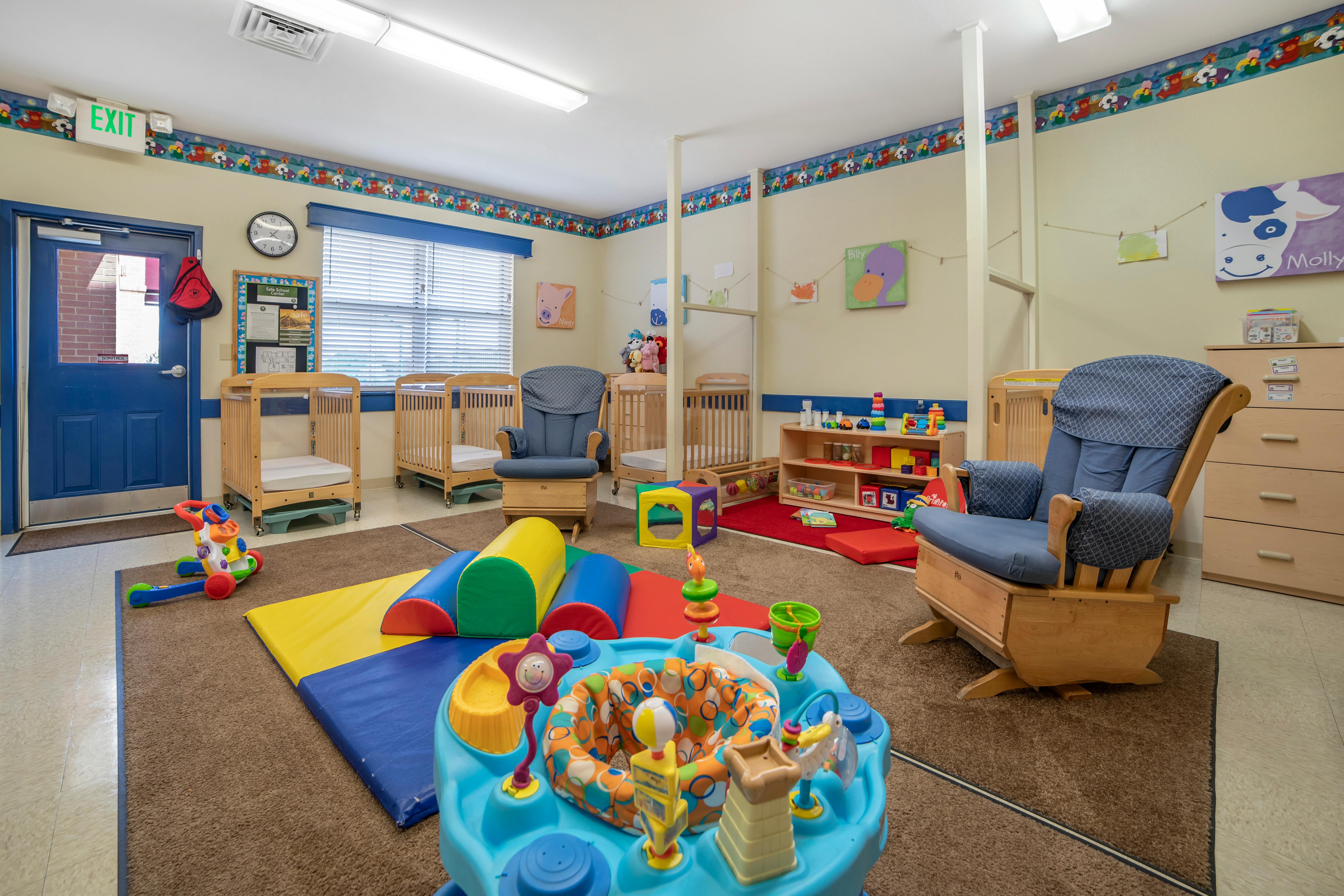 A childcare room with cribs, rocking chairs, and colorful play mats