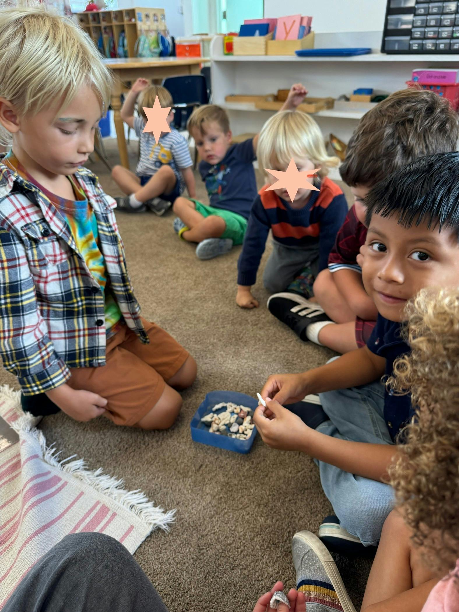 Children sitting on the floor in a classroom, one holding small objects