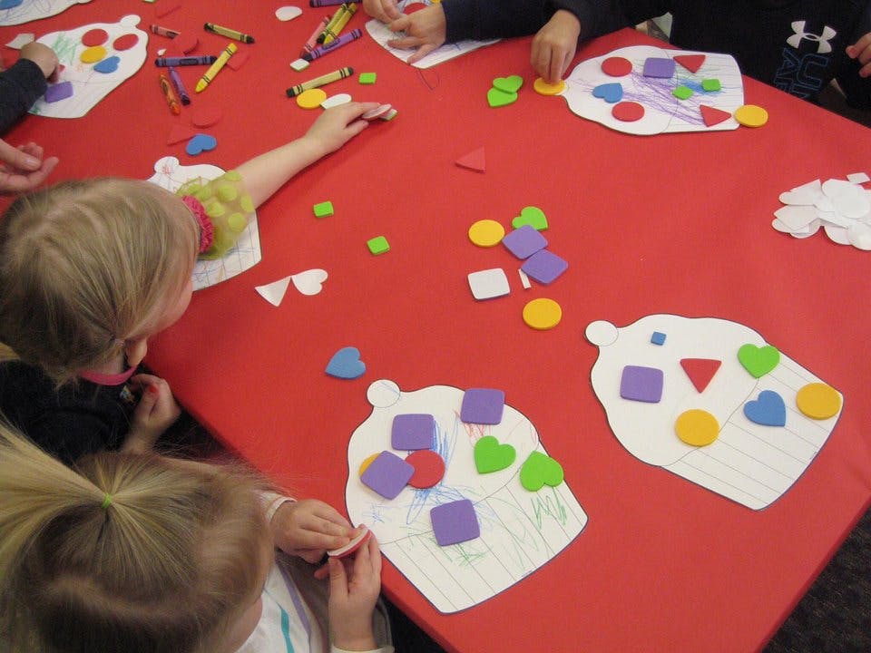 Children doing crafts with foam shapes on a red table