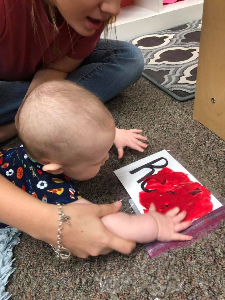 Person and child on floor, child touching red paint in a bag with letter R