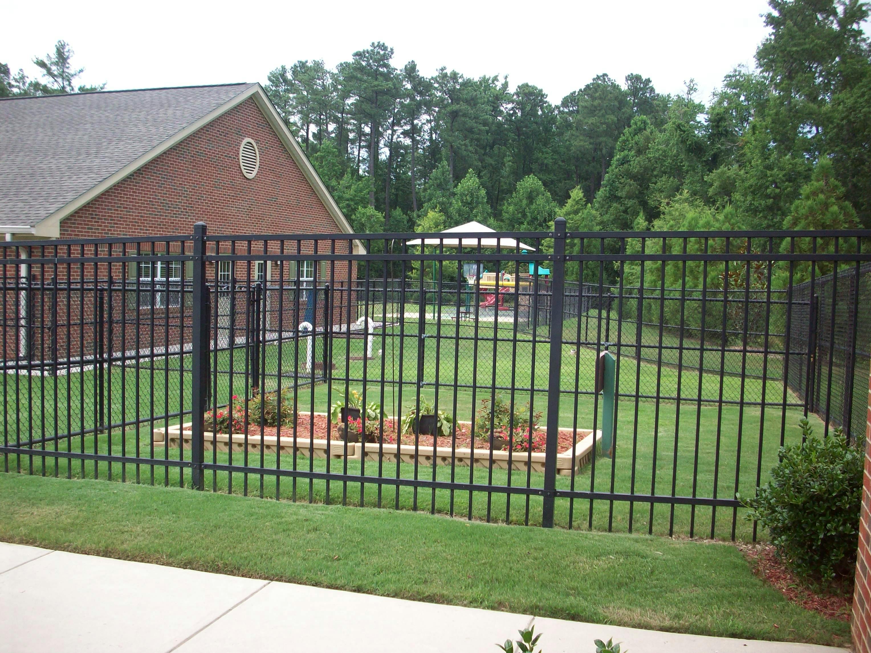 Black metal fence enclosing a grassy yard with a brick building