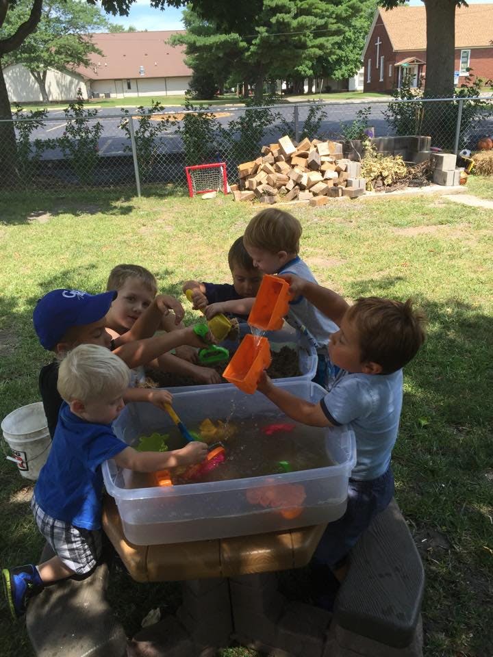 Children playing with water and toys in a plastic bin outdoors